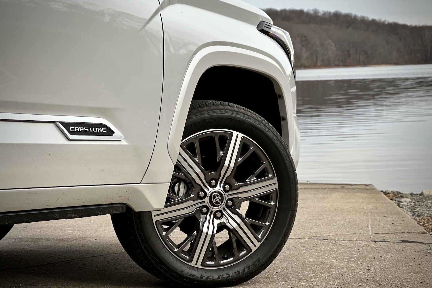 Close up of front wheel on 2022 Toyota Tundra Hybrid Capstone parked on a boat ramp in front of a lake.