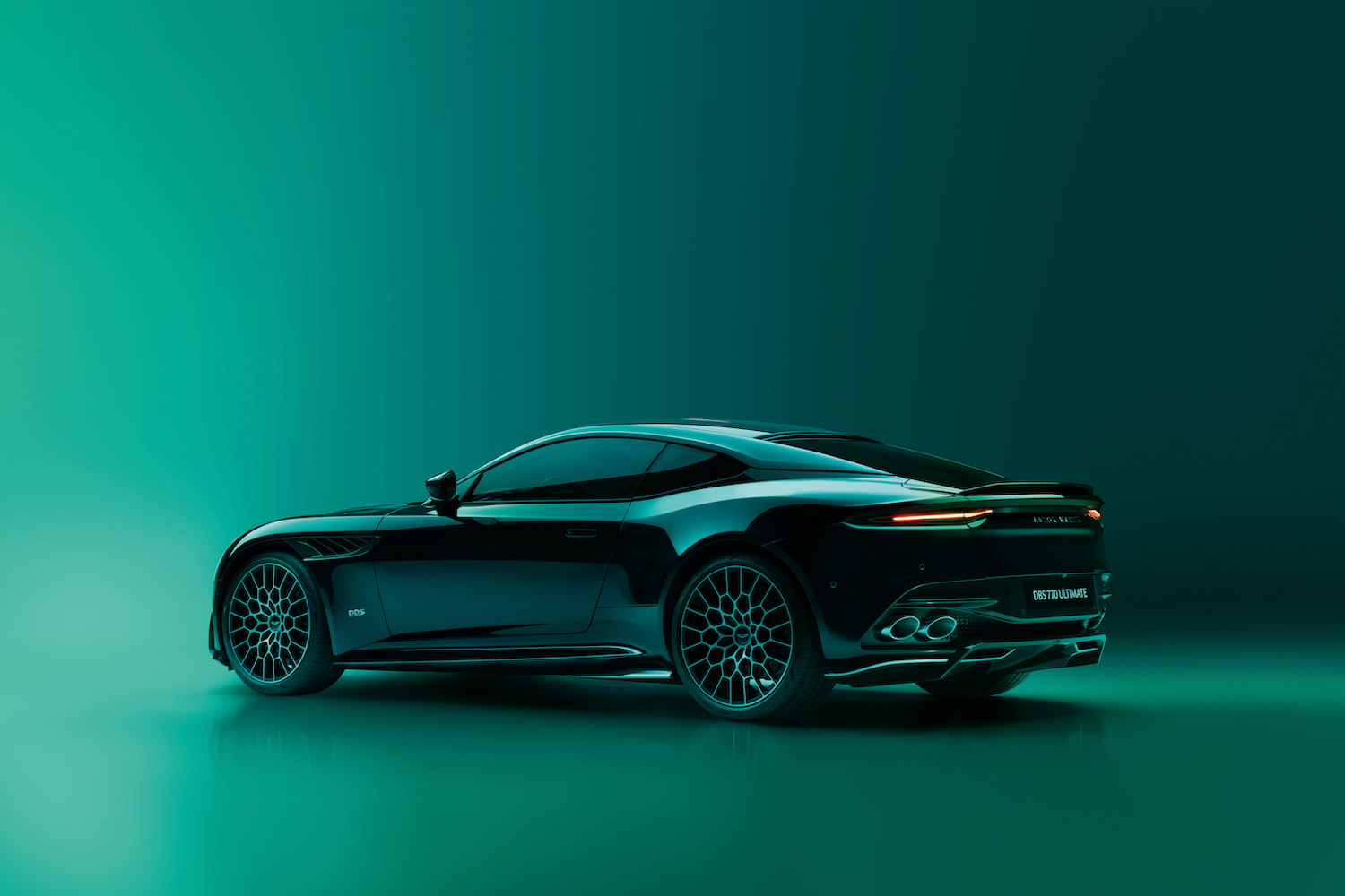 Rear end angle of 2023 Aston Martin DBS 770 Ultimate in front of a green studio wall.