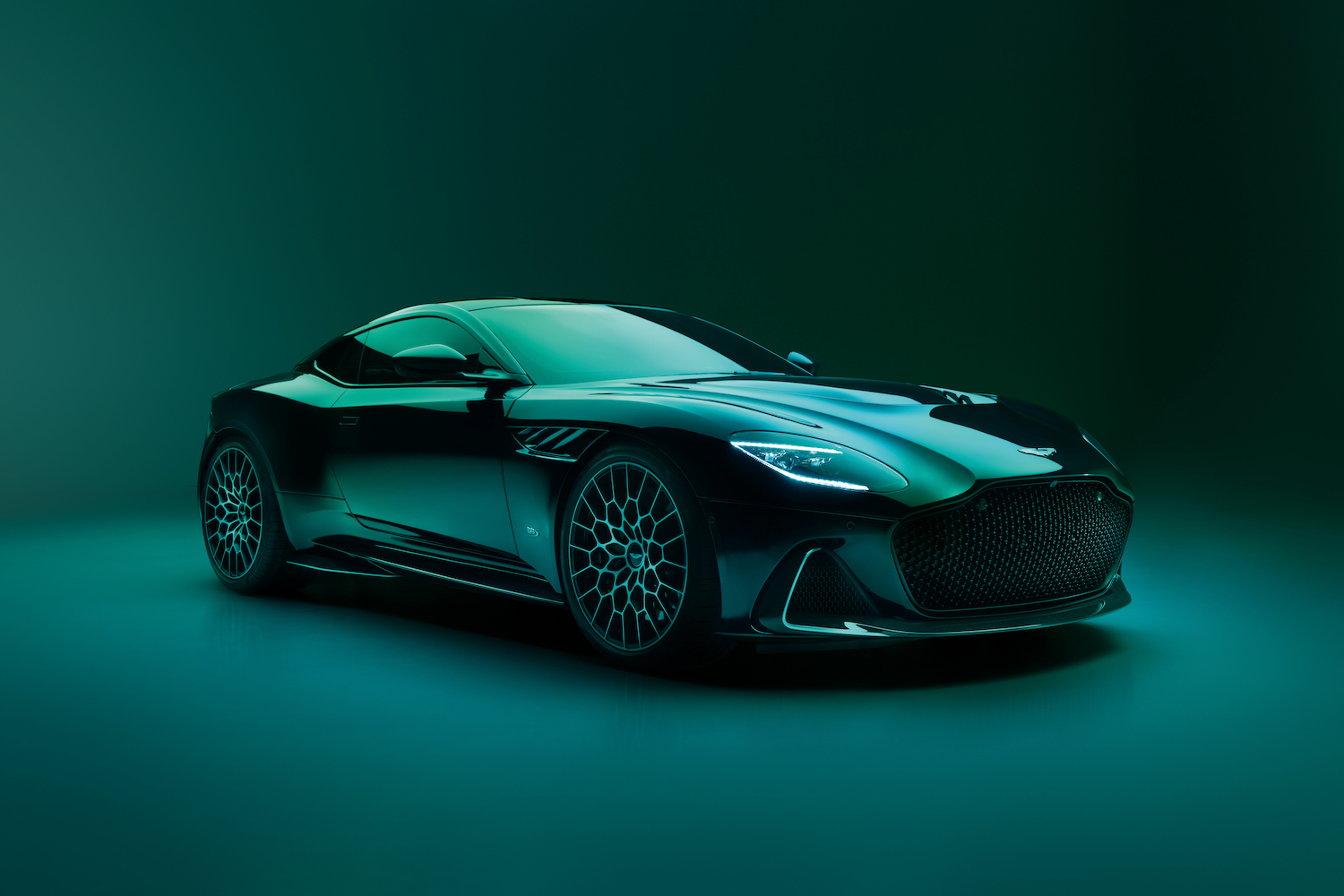 Front end angle of 2023 Aston Martin DBS 770 Ultimate from passenger's side in a green studio with dramatic lighting.