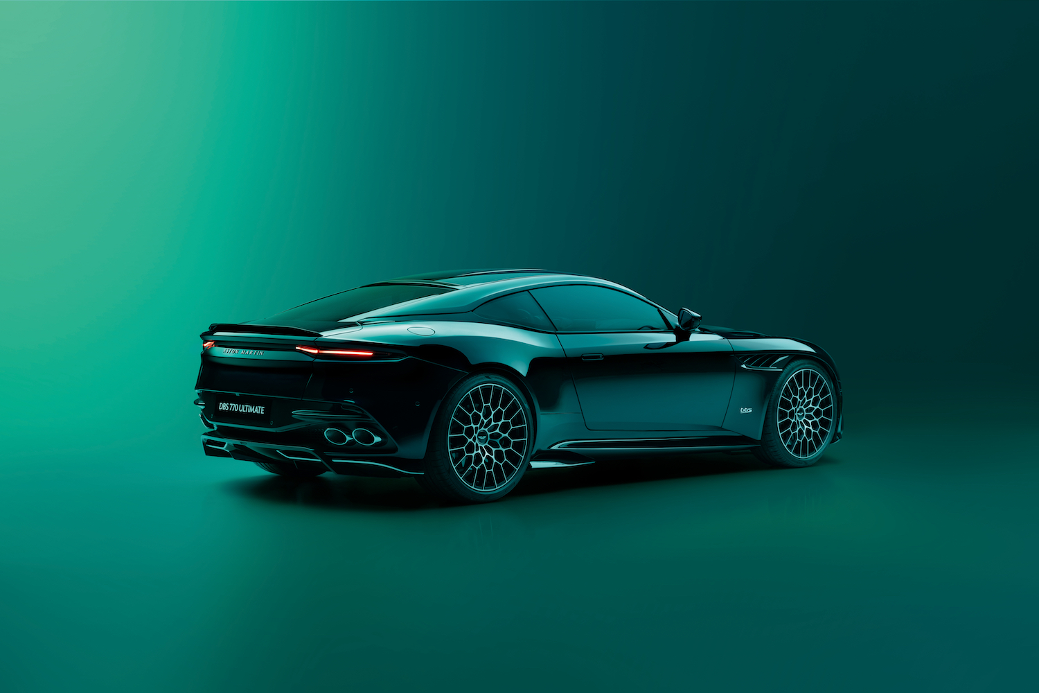 Rear end angle of 2023 Aston Martin DBS 770 Ultimate from passenger's side in a green studio with green walls.