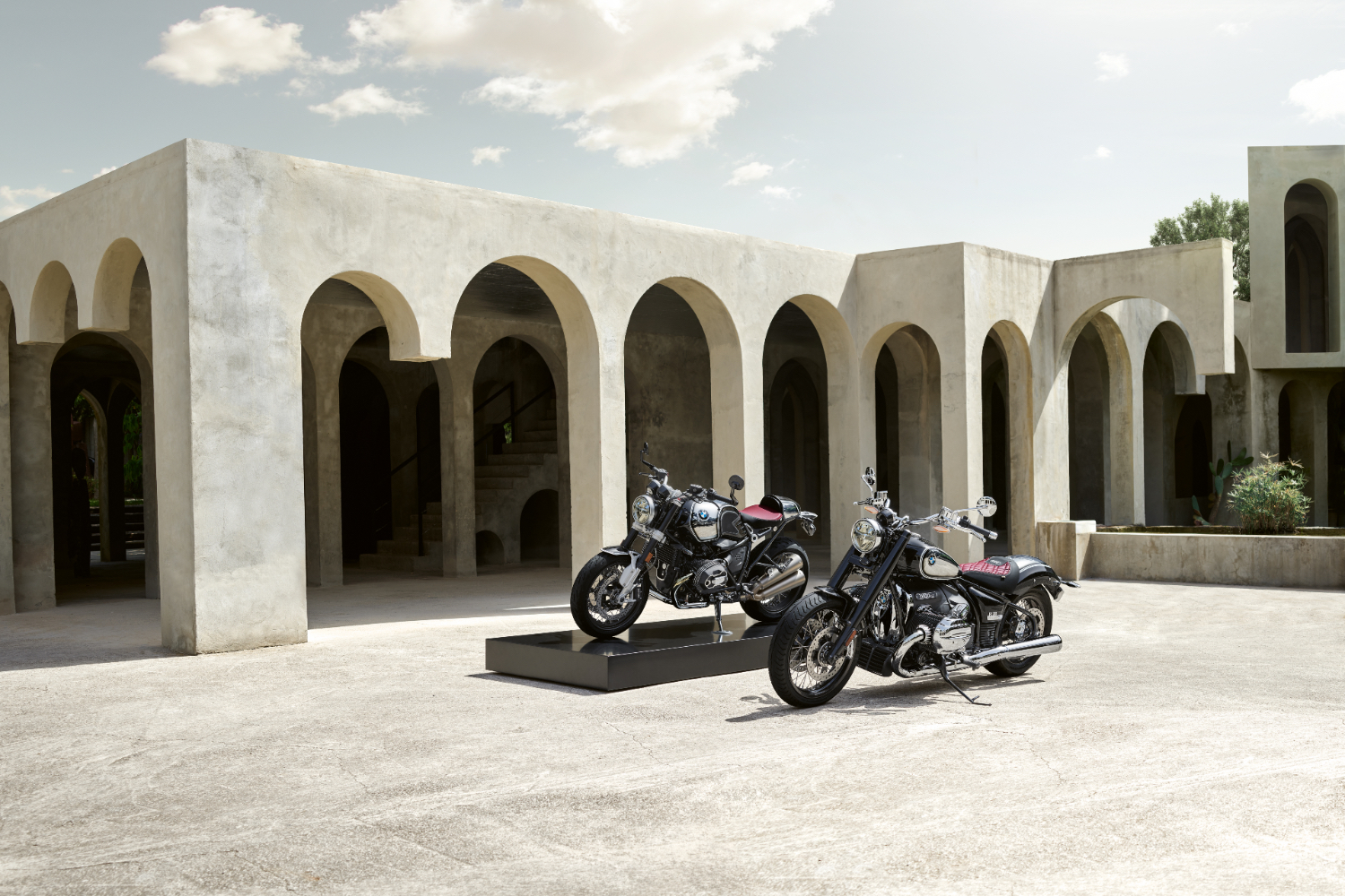 2023 BMW R 18 and R nineT 100 Years Editions parked in front of a villa with clouds and sun in the back.