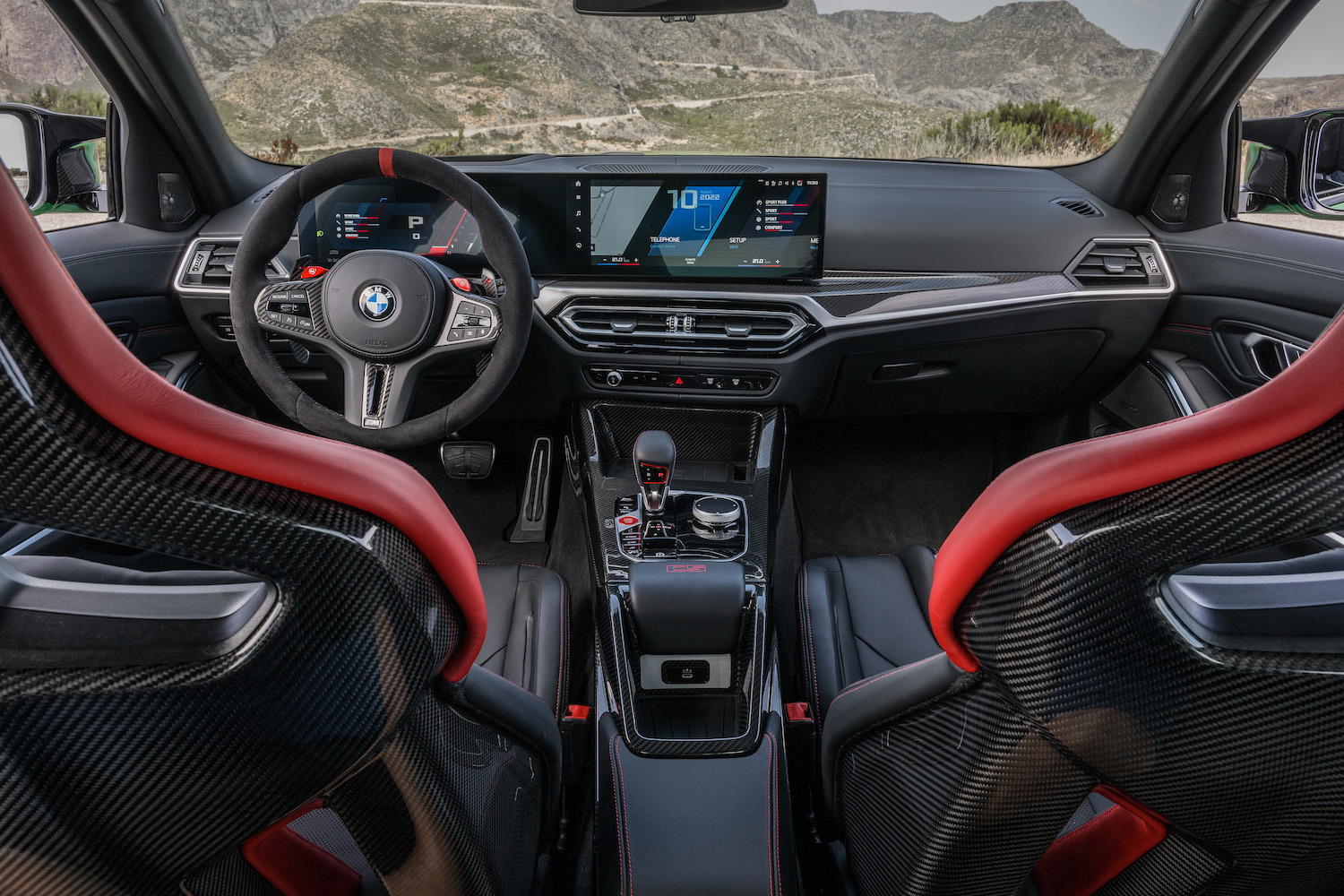 View of 2024 BMW M3 CS dashboard from the rear seats with mountains in the back.
