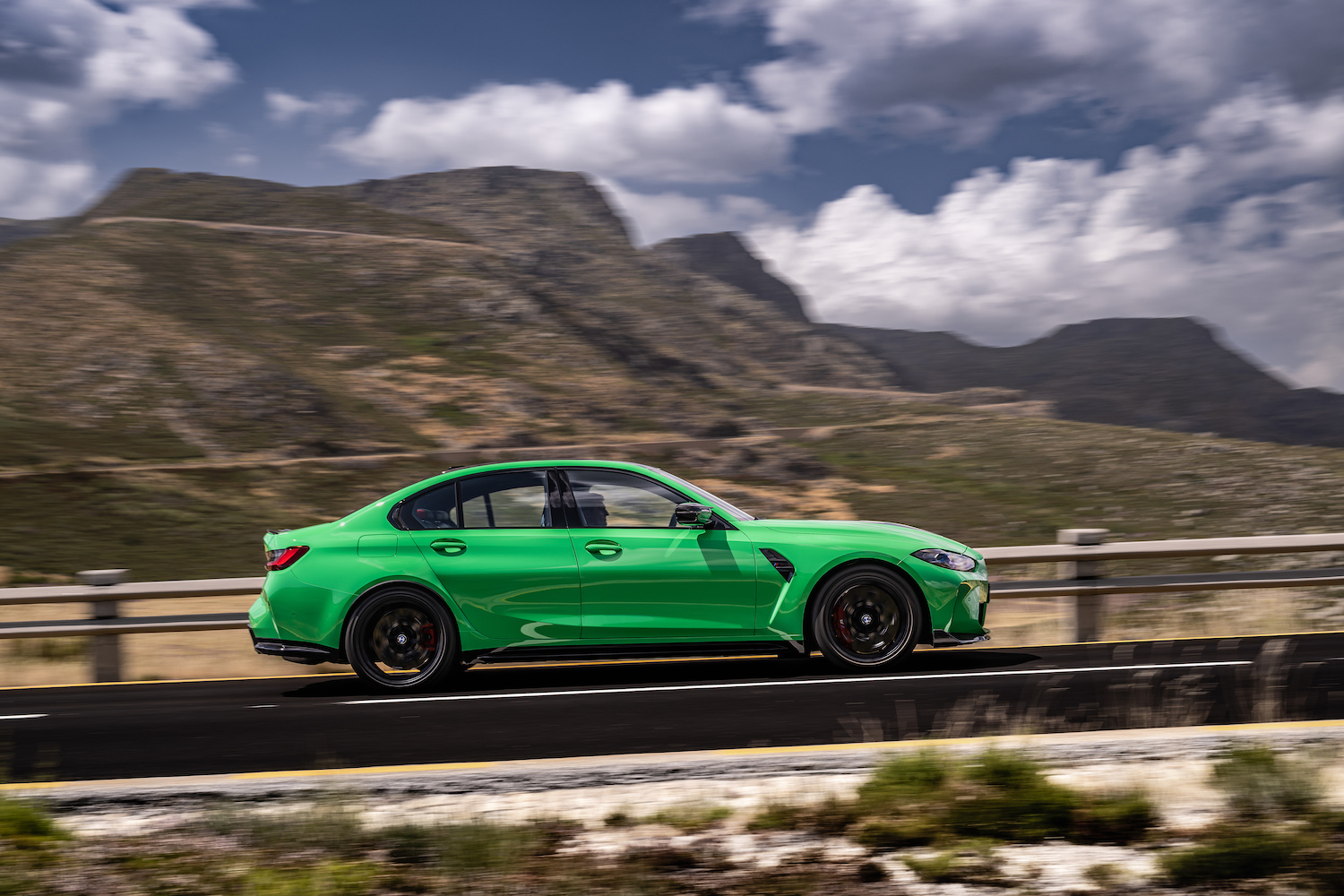 Side profile of 2024 BMW M3 CS parked on the side of the road in front of mountains.