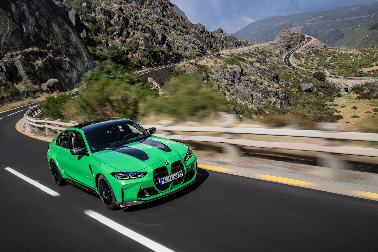 Close up of front end on 2024 BMW M3 CS driving down a windy road with a mountain in the back.