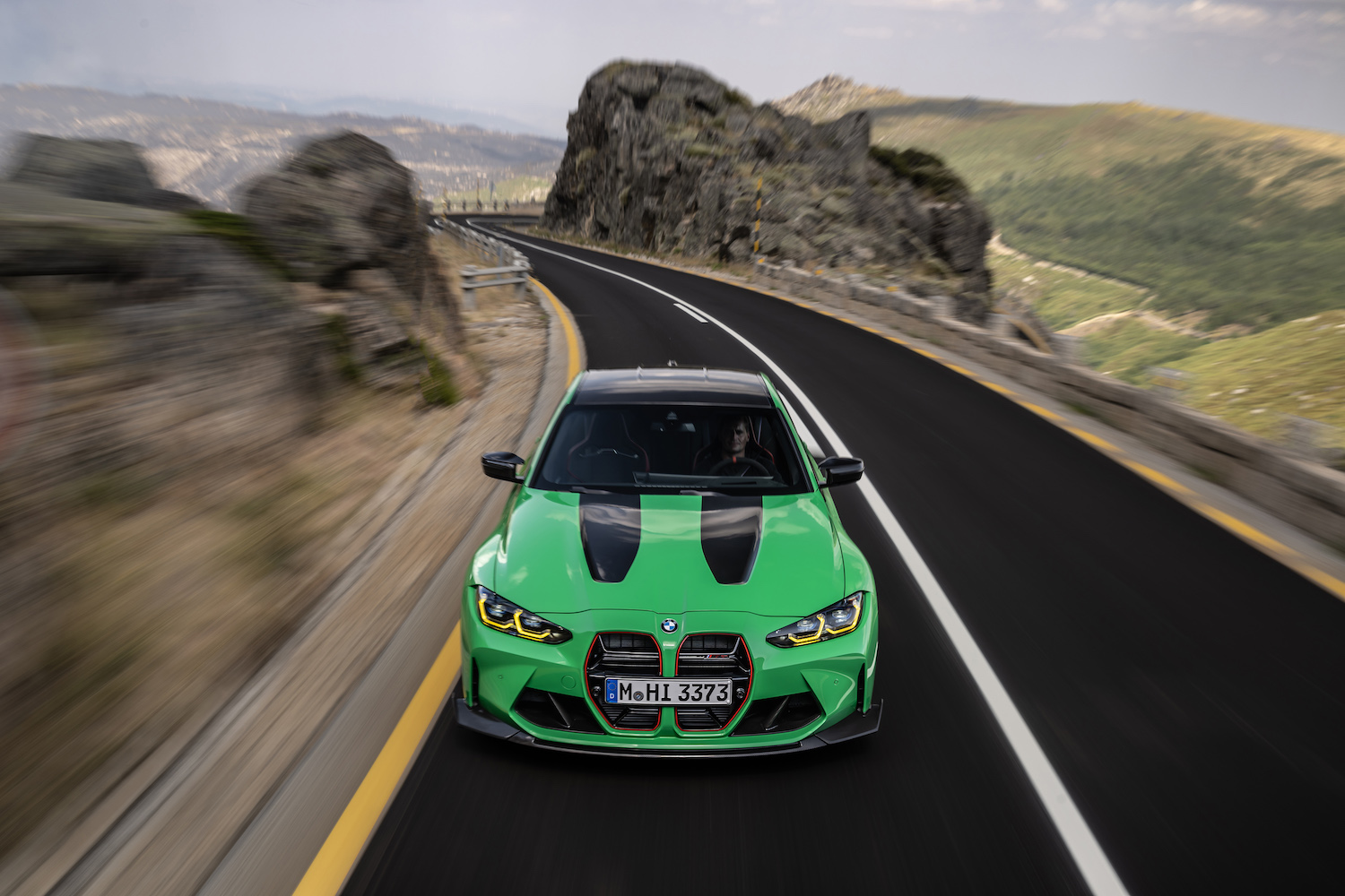 Close up of front end of 2024 BMW M3 CS driving down a windy road with mountain in the back.