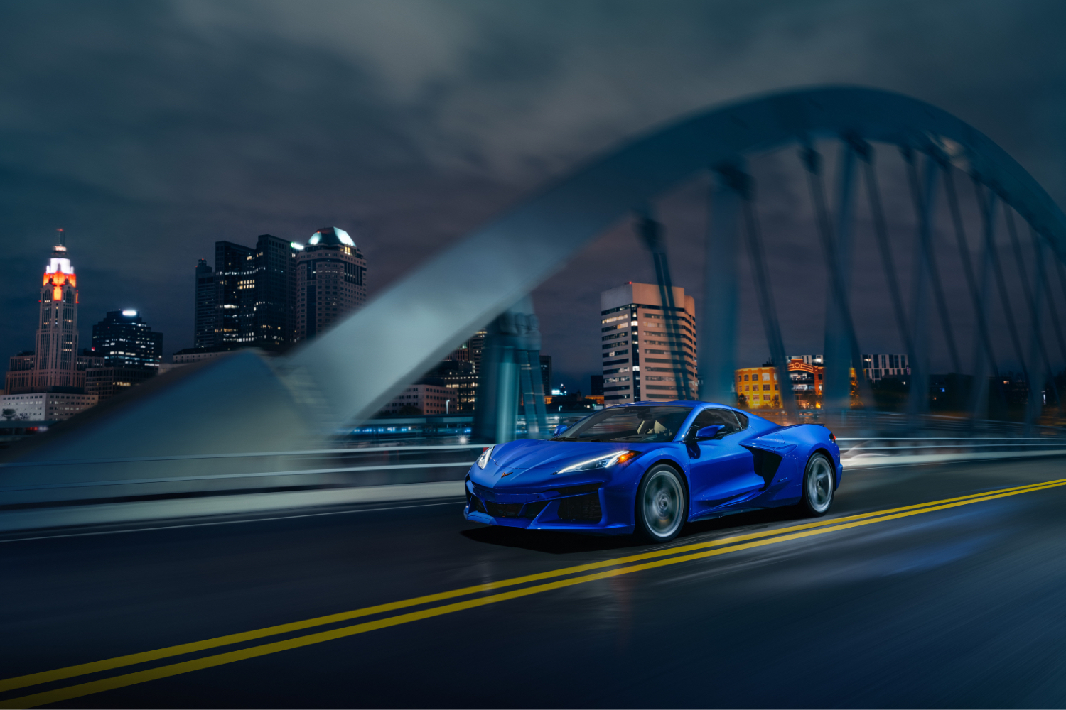 2024 Chevrolet Corvette E-Ray front end angle driving on a bridge with Detroit city skyline in the back ground.