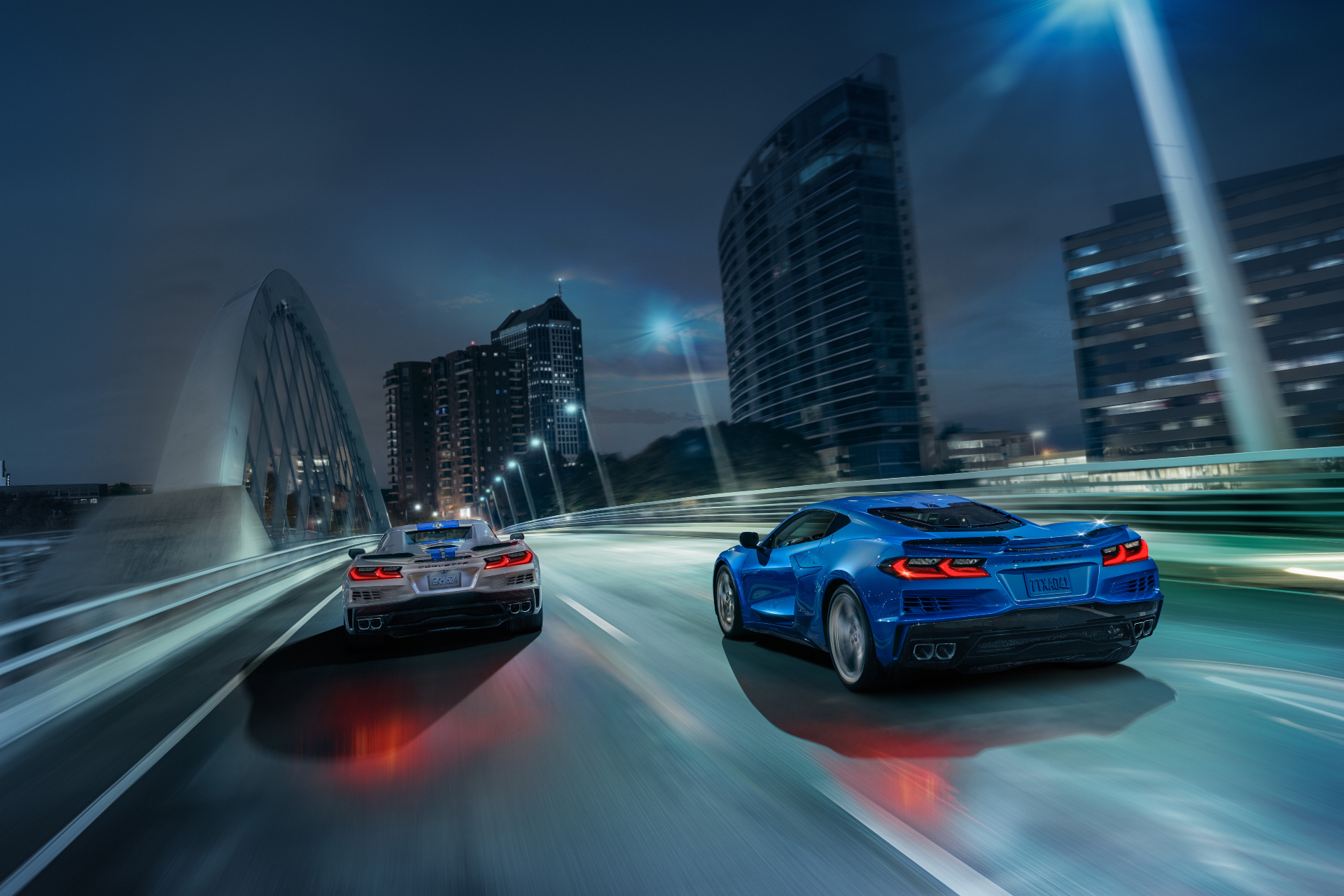 Rear ends of 2024 Chevrolet Corvette E-Rays driving down the street with Detroit city in the back.