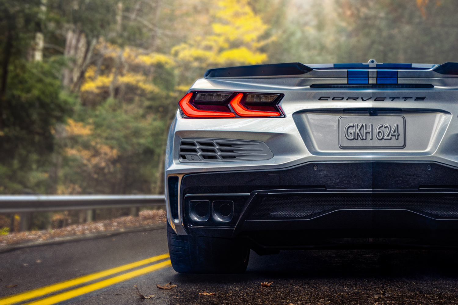 Close up of rear end on 2024 Chevrolet Corvette E-Ray parked on the side of the road with trees in the back.