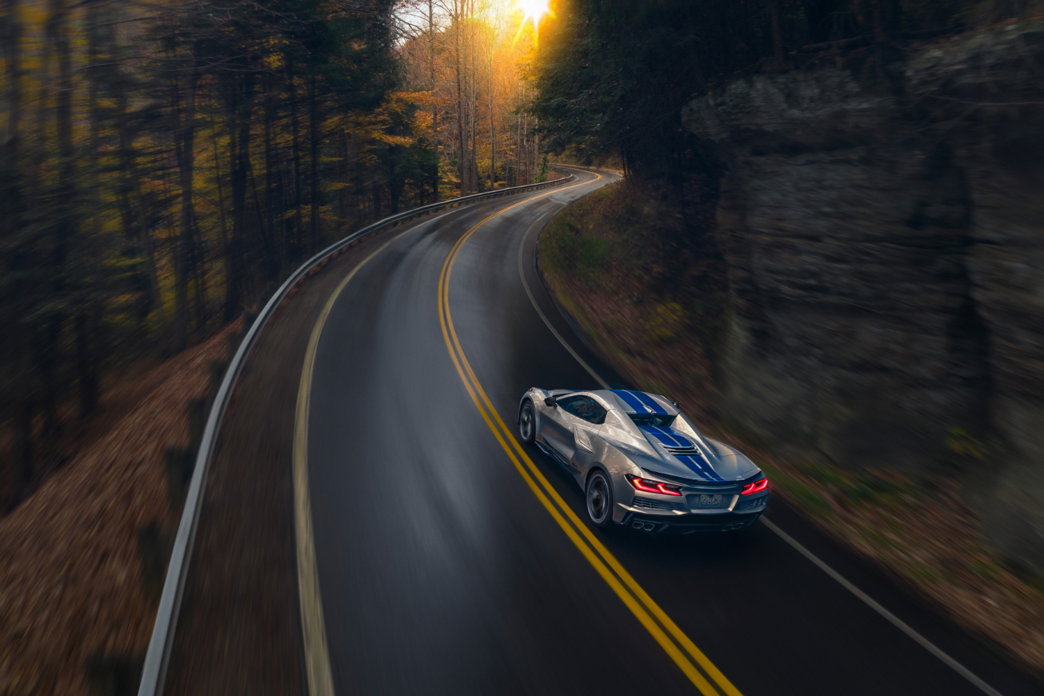 Rear end angle of 2024 Chevrolet Corvette E-Ray driving up a windy road with trees in the back.