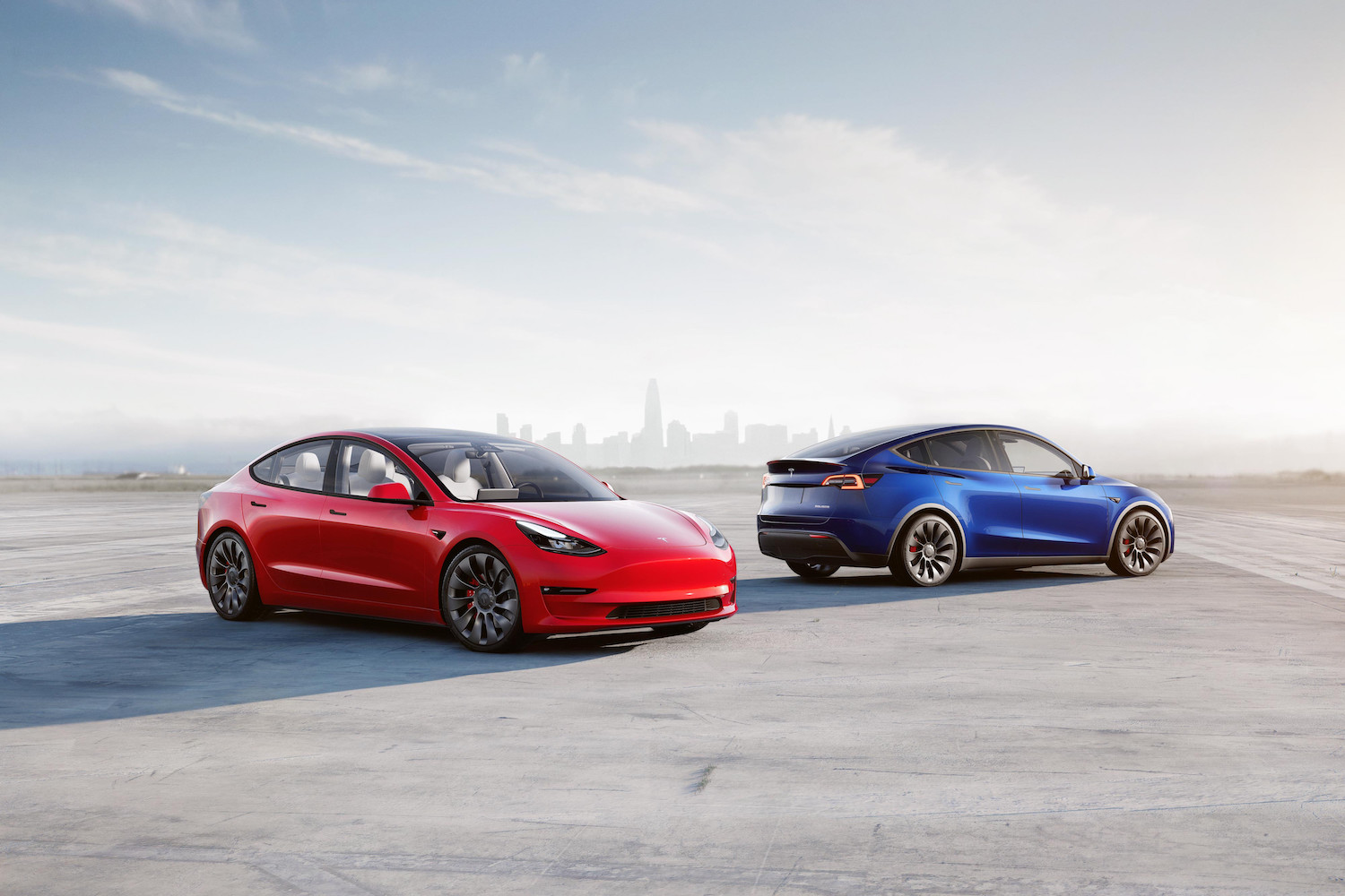 Tesla Model 3 and Model Y parked in front of a city skyline on a runway.