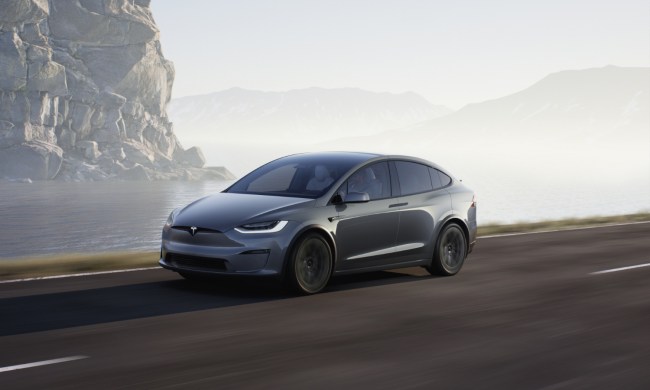 Tesla Model X front end angle driving down the road with mountain cliffs in the back.
