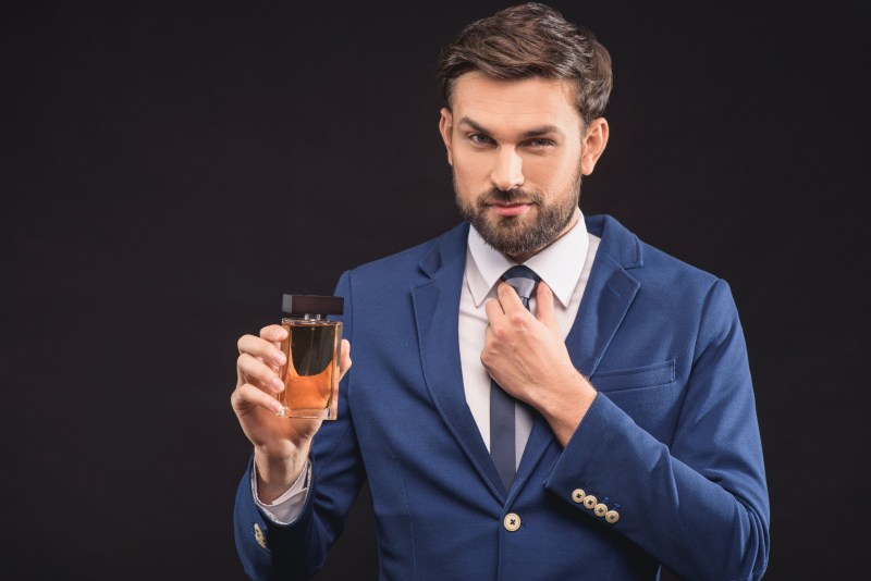 A man in a suit holding a bottle of cologne