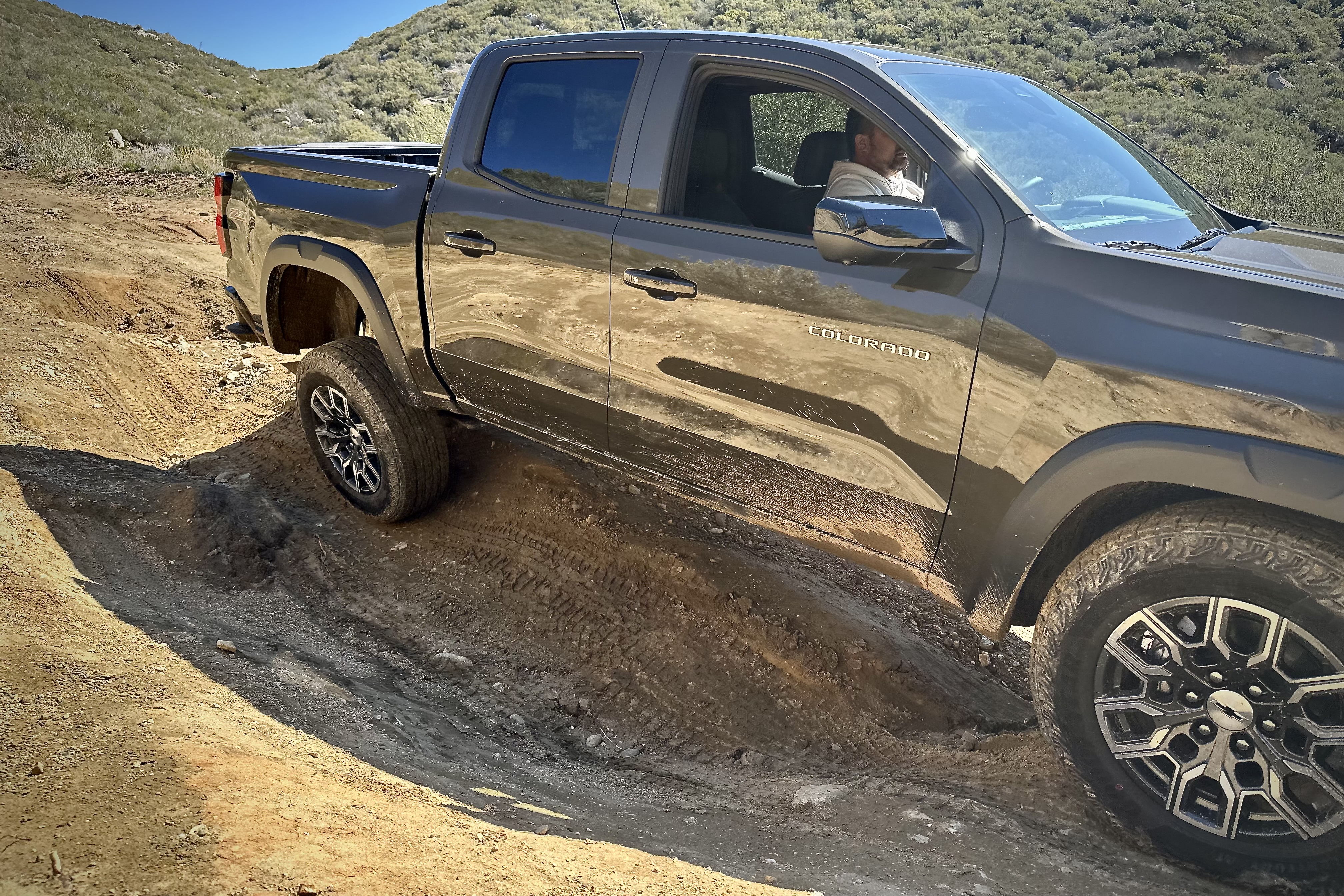 Side profile of the 2023 Chevrolet Colorado Trail Boss lifting a rear tire while off-roading on a dirt trail.