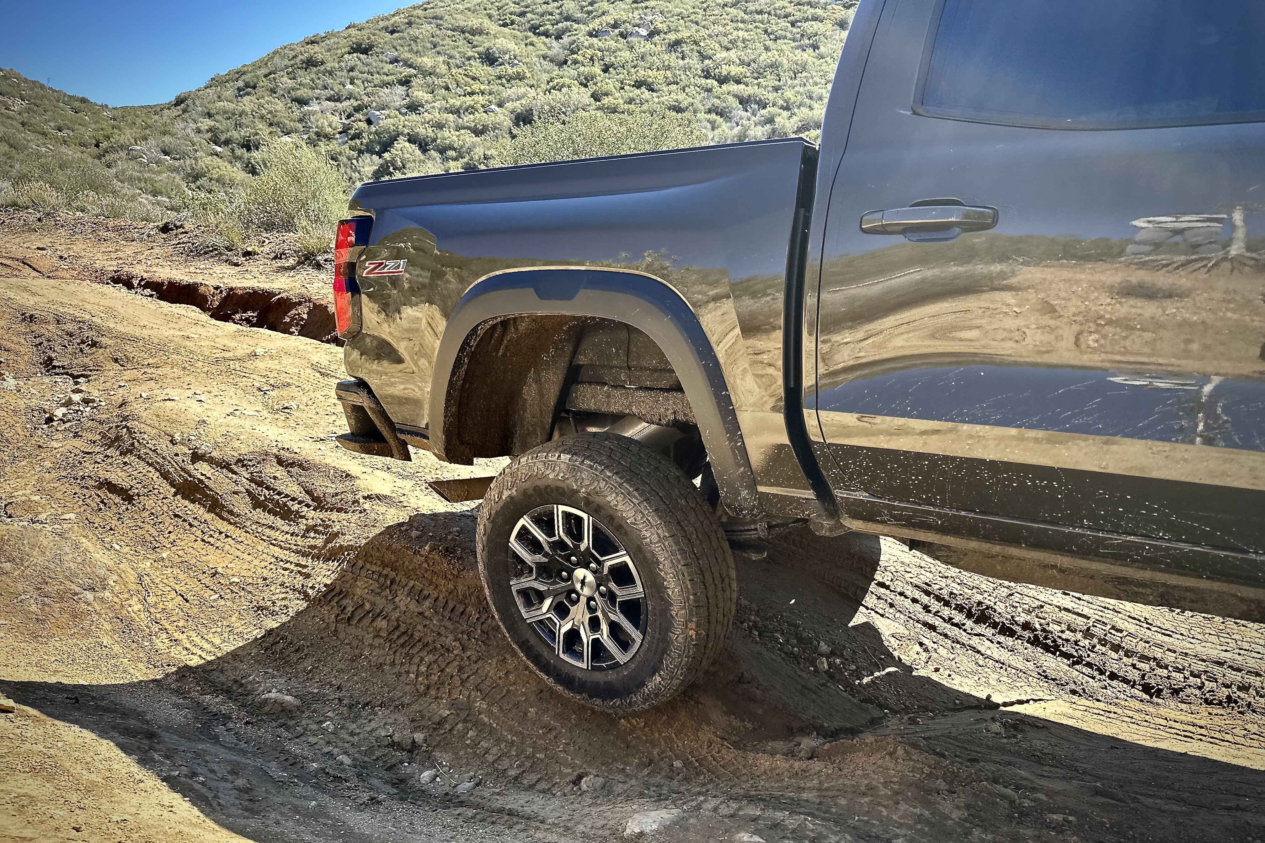 2023 Chevrolet Colorado Trail Boss off-roading close up with there rear wheel in the air with mountains in the back.