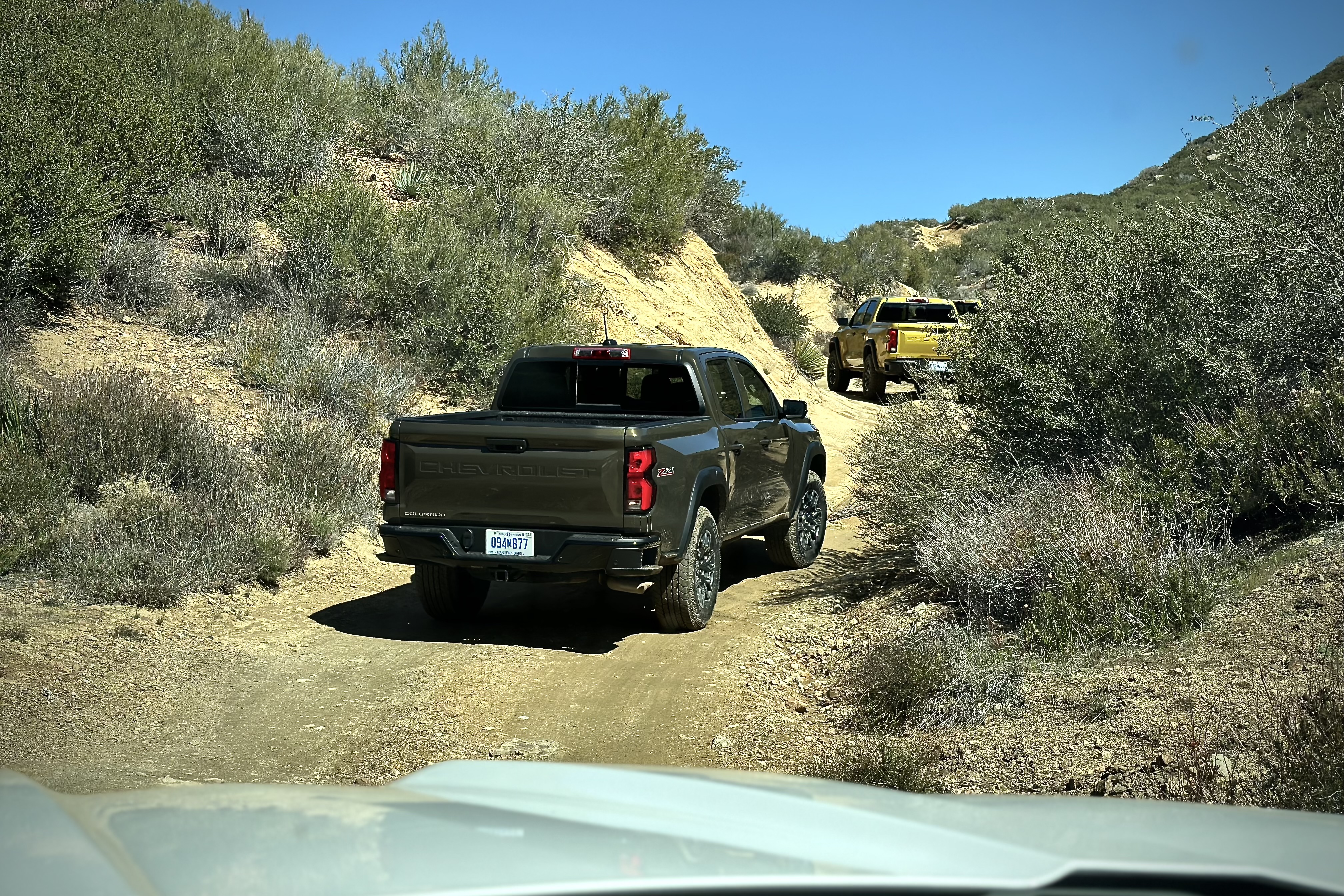 2023 Chevrolet Colorado Trail Boss off-roading on a dirt trail with mountains and bushes in the back.