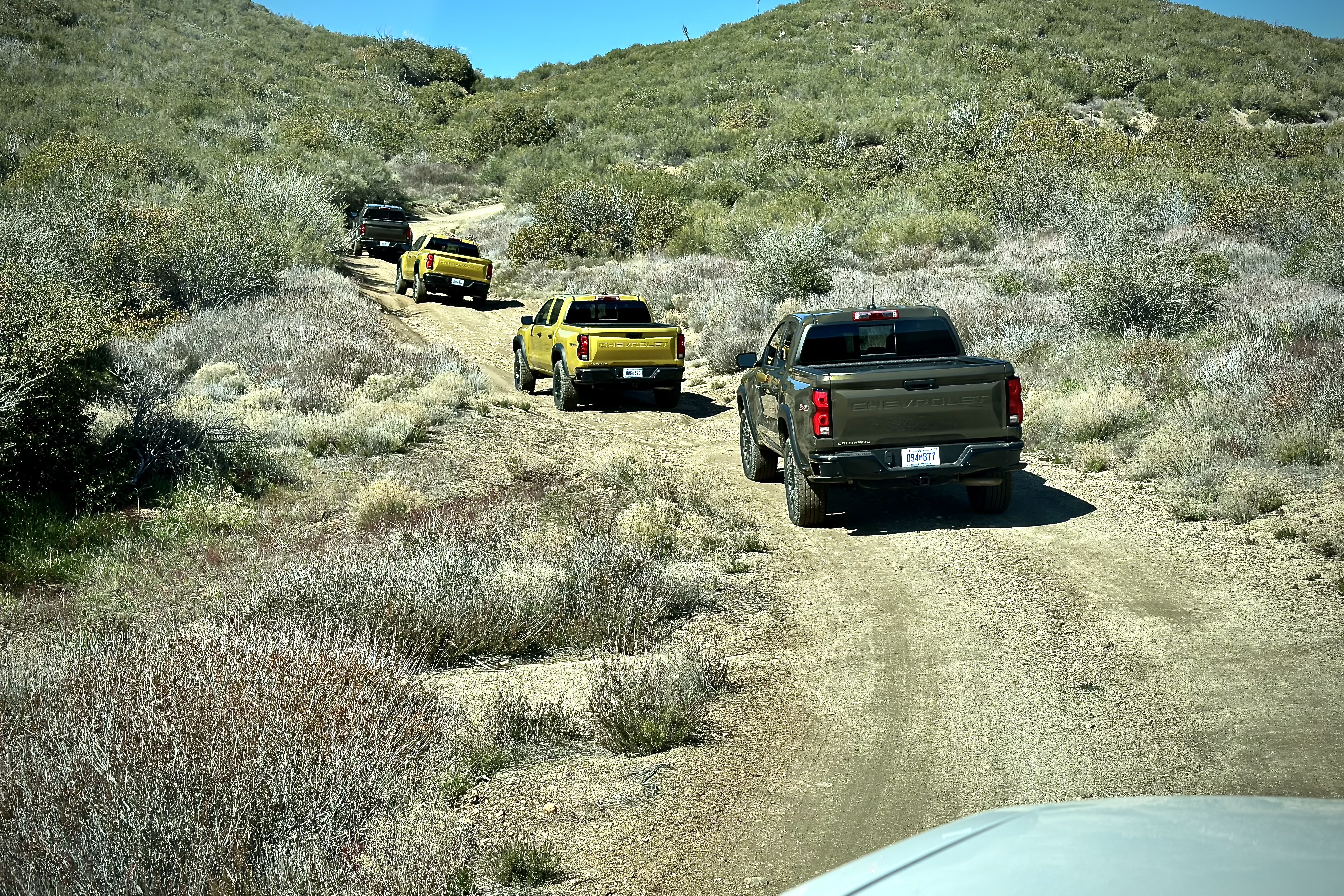 2023 Chevrolet Colorado Trail Boss off-roading on a dirt trail with mountains and bushes in the back.