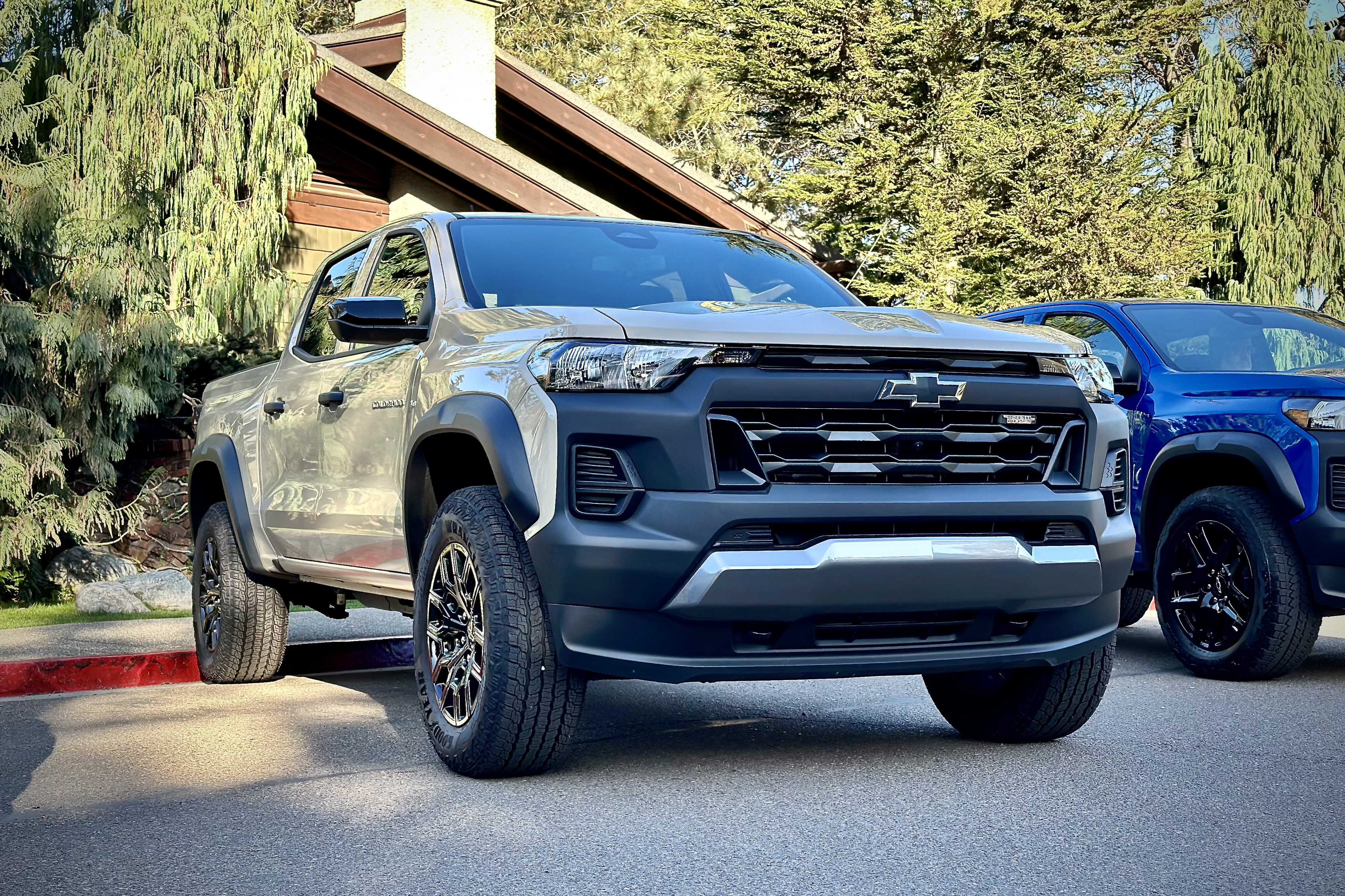 Front end close up of the 2023 Chevrolet Colorado Trail Boss parked in front of a lodge with trees.