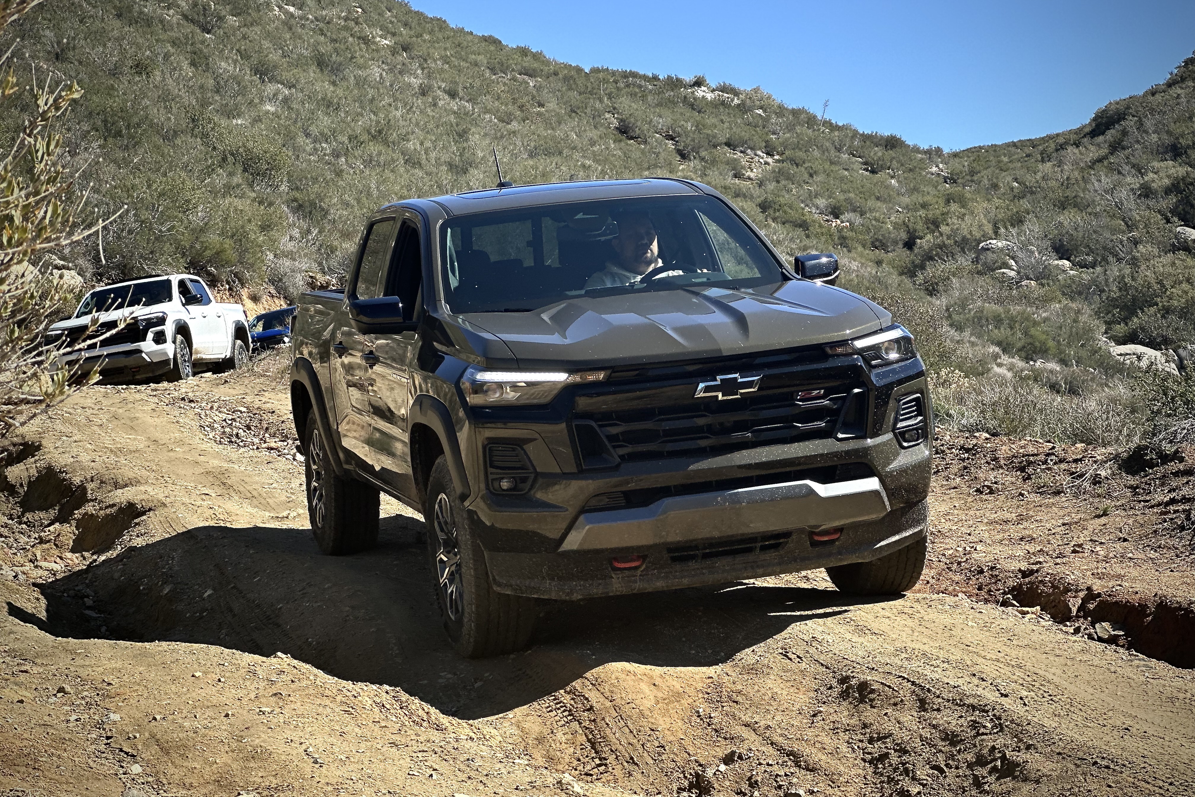 Close up of 2023 Chevrolet Colorado Trail Boss tackling a dirt trail with mountains in the back.