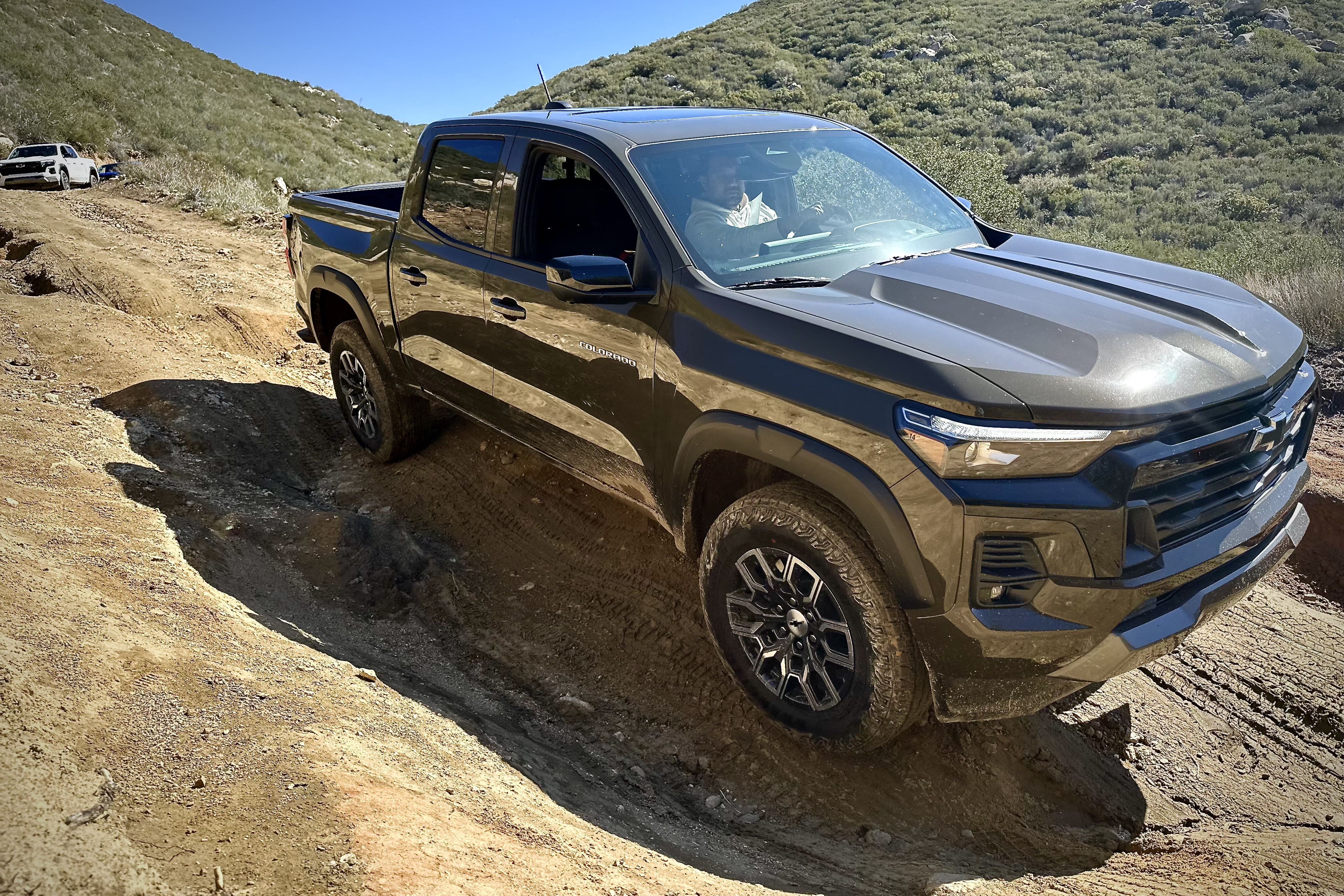 Close up of the side profile of the 2023 Chevrolet Colorado Trail Boss tackling a deep rut on a dirt trail with mountains the th
