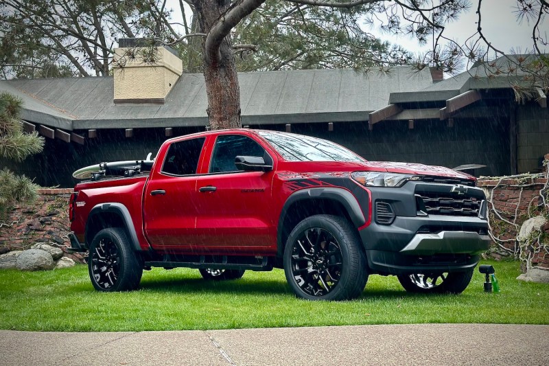 2023 Chevrolet Colorado Trail Boss front end angle from passenger's side parked on a grass lawn in front of a lodge on a rainy day.