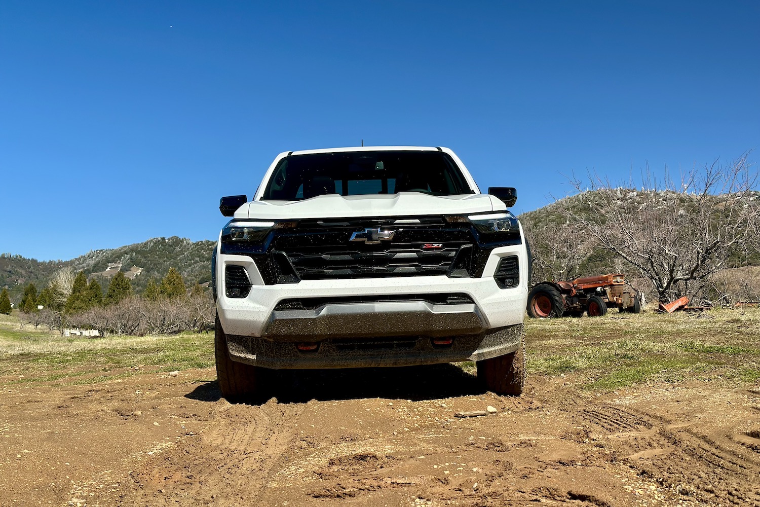 Front end close up of the 2023 Chevrolet Colorado Z71 parked in a muddy field with mountains in the back.