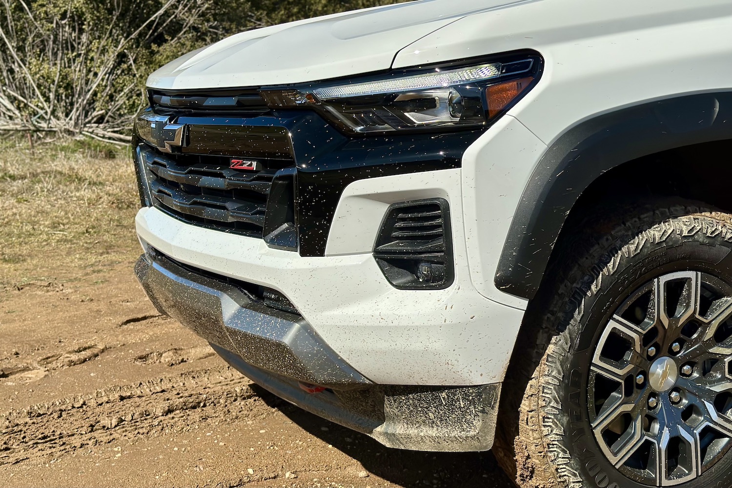 Close up of the headlights, grille, and front fascia on the 2023 Chevrolet Colorado Z71 parked in a muddy field.