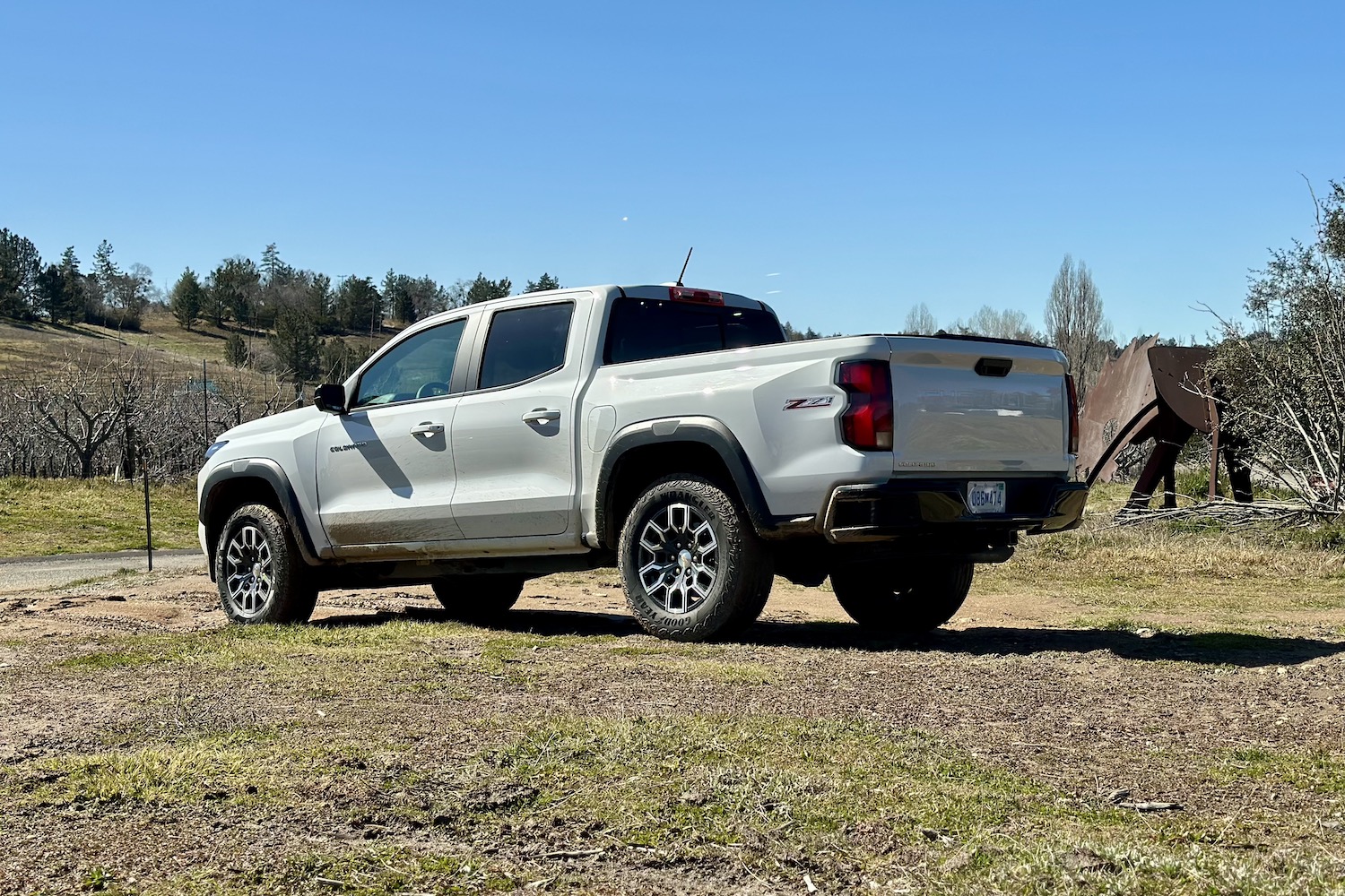 Rear end angle of the 2023 Chevrolet Colorado Z71 parked in a muddy field with trees in the back.