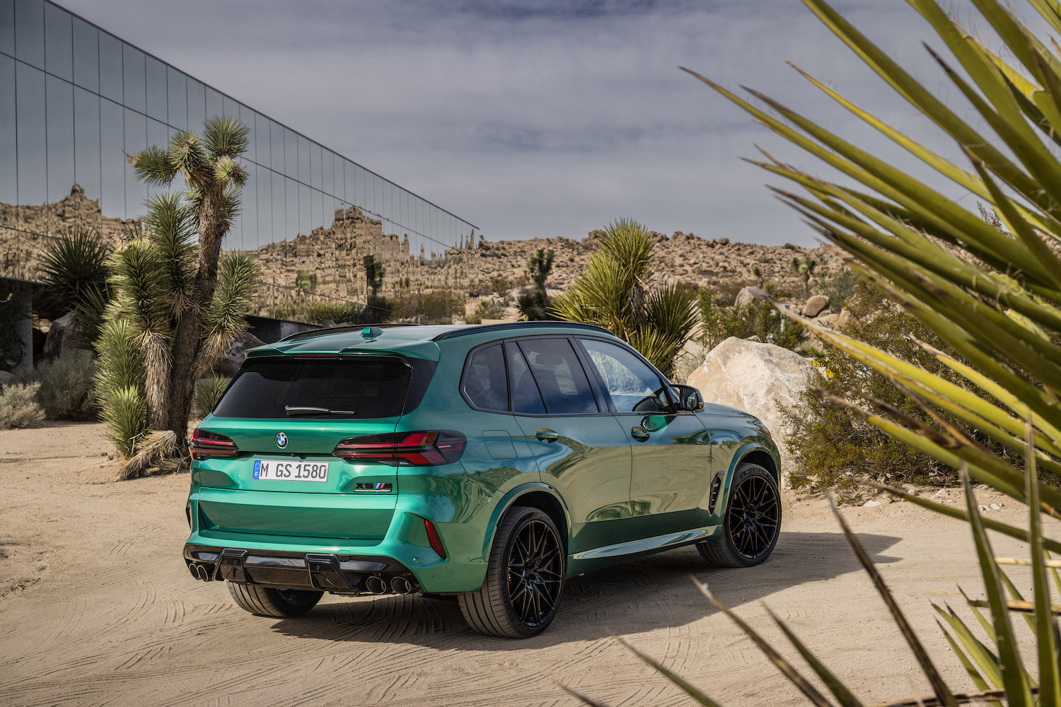 Rear end angle of the 2024 BMW X5 M Competition parked in front of a glass building in the desert.