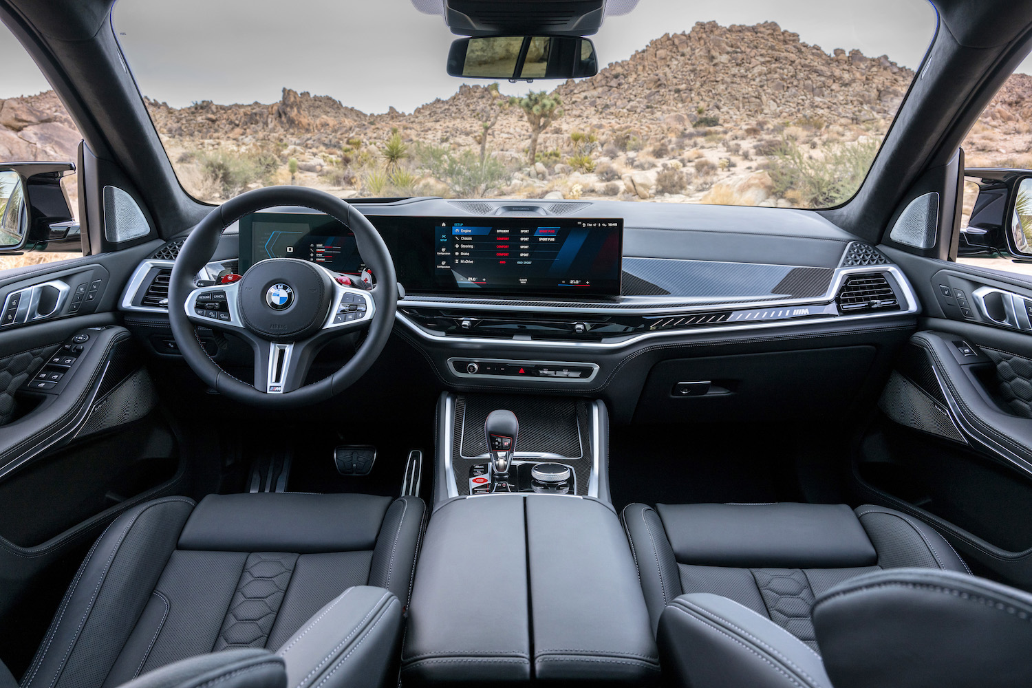 Dashboard close up in the 2024 BMW X5 M Competition from the rear seats with desert in the back.