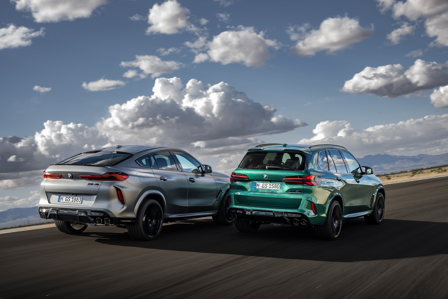 2024 BMW X5 M and X6 M Competition rear end angle parked on the side of the road in front of clouds.