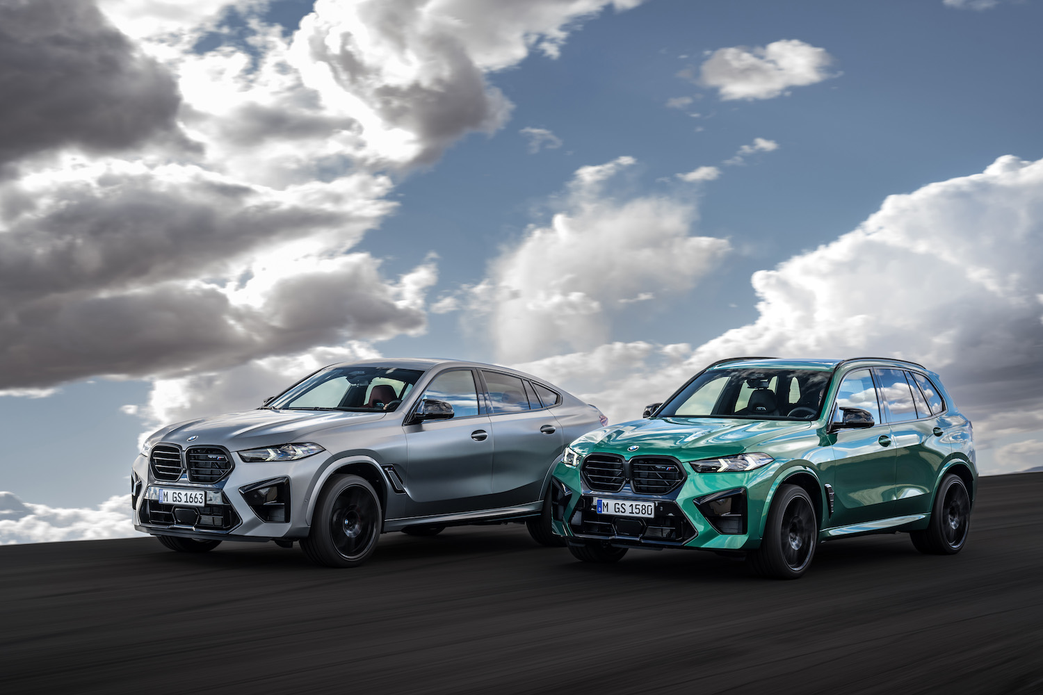 2024 BMW X5 M and X6 M Competition front end angle parked on the side of the road in front of clouds.