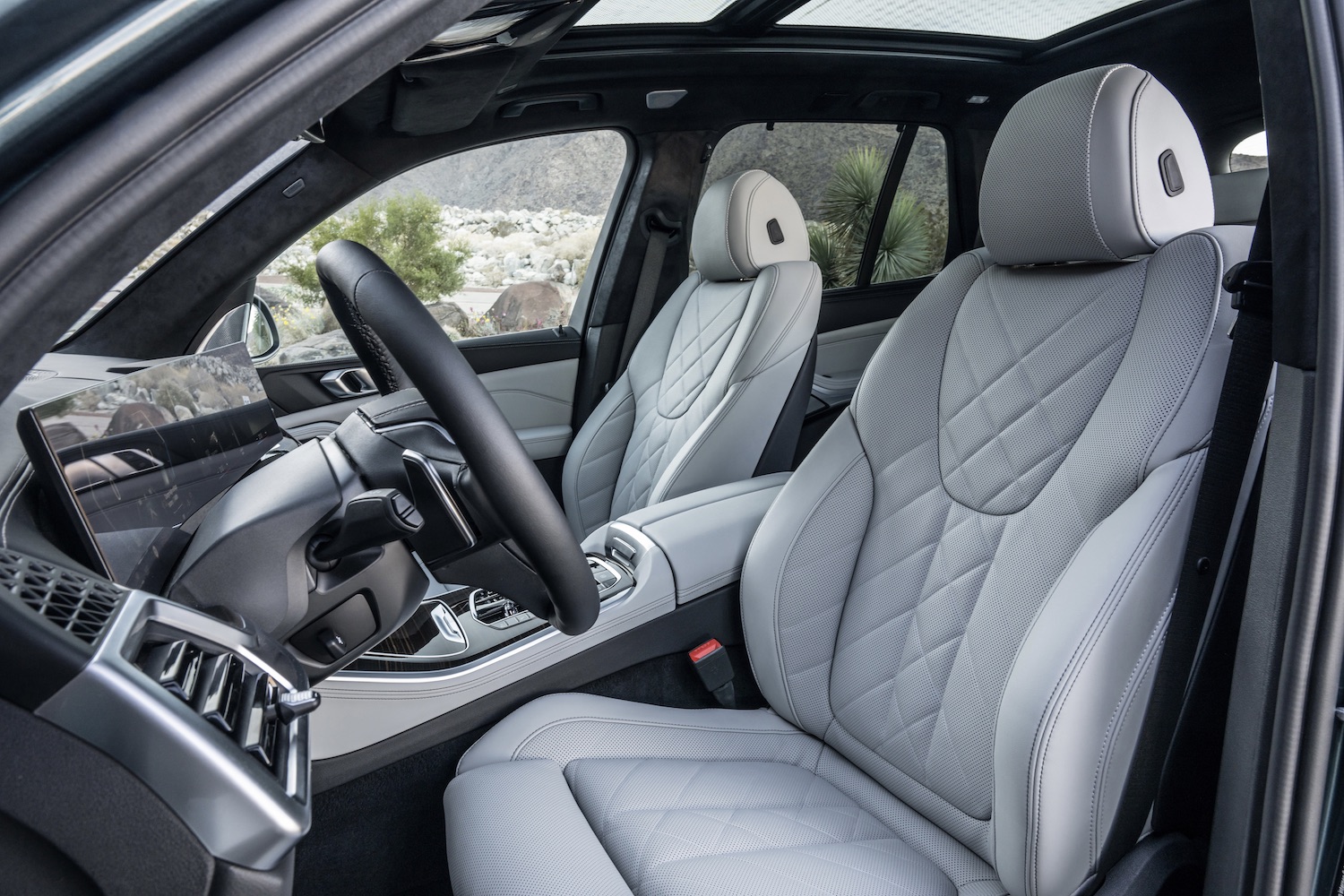 Front seats in the 2024 BMW X5 and X6 from outside the driver's side with bushes and dirt in the back.