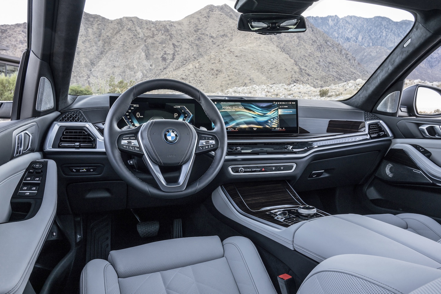 Close up of steering wheel and dashboard in the 2024 BMW X5 and X6 from the driver's seat with mountains in the back.