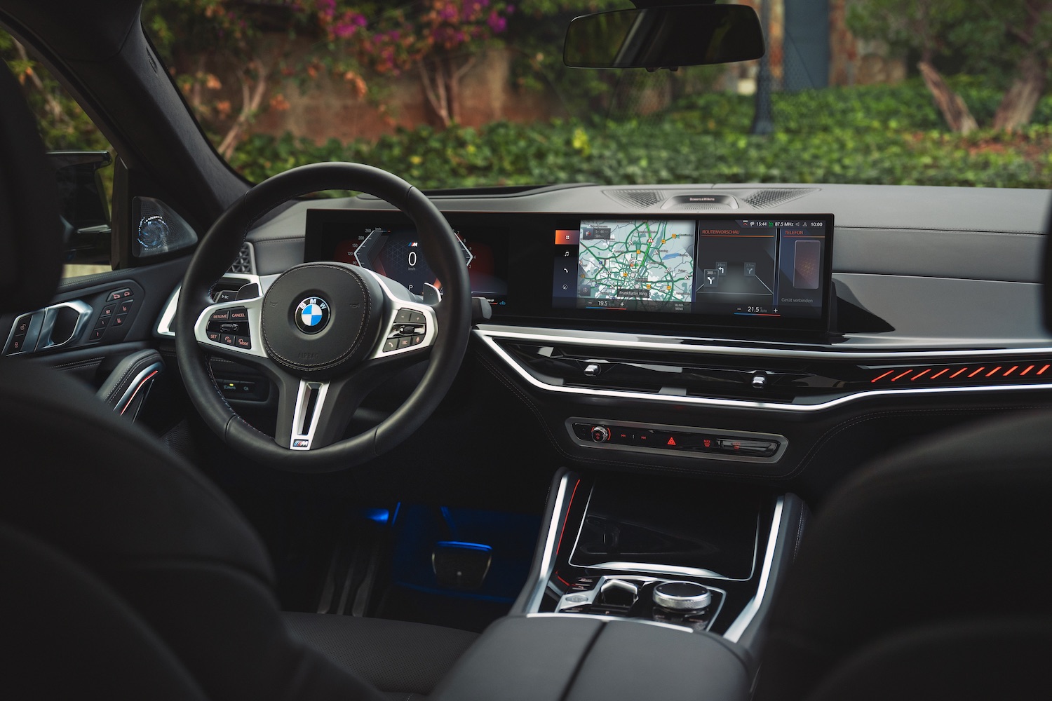 Close up of the steering wheel and dashboard in the 2024 BMW X5 and X6 from the rear seats with green grass in the back.