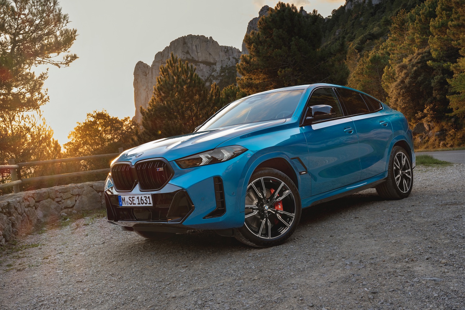 Front end angle of 2024 BMW X6 parked on the side of the road in front of a mountain during a sunrise.
