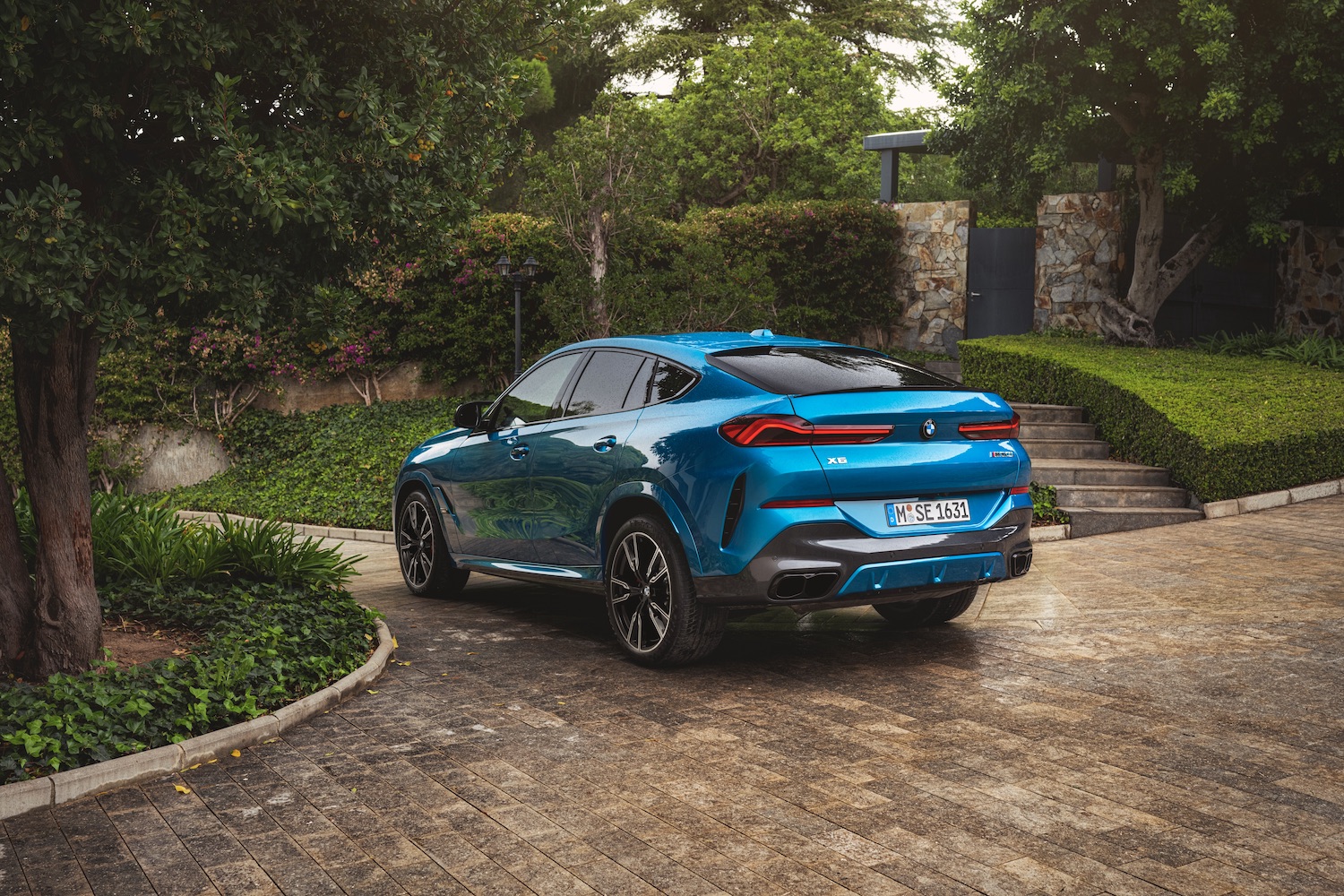 Rear end angle of the 2024 BMW X6 parked on a brick lane.