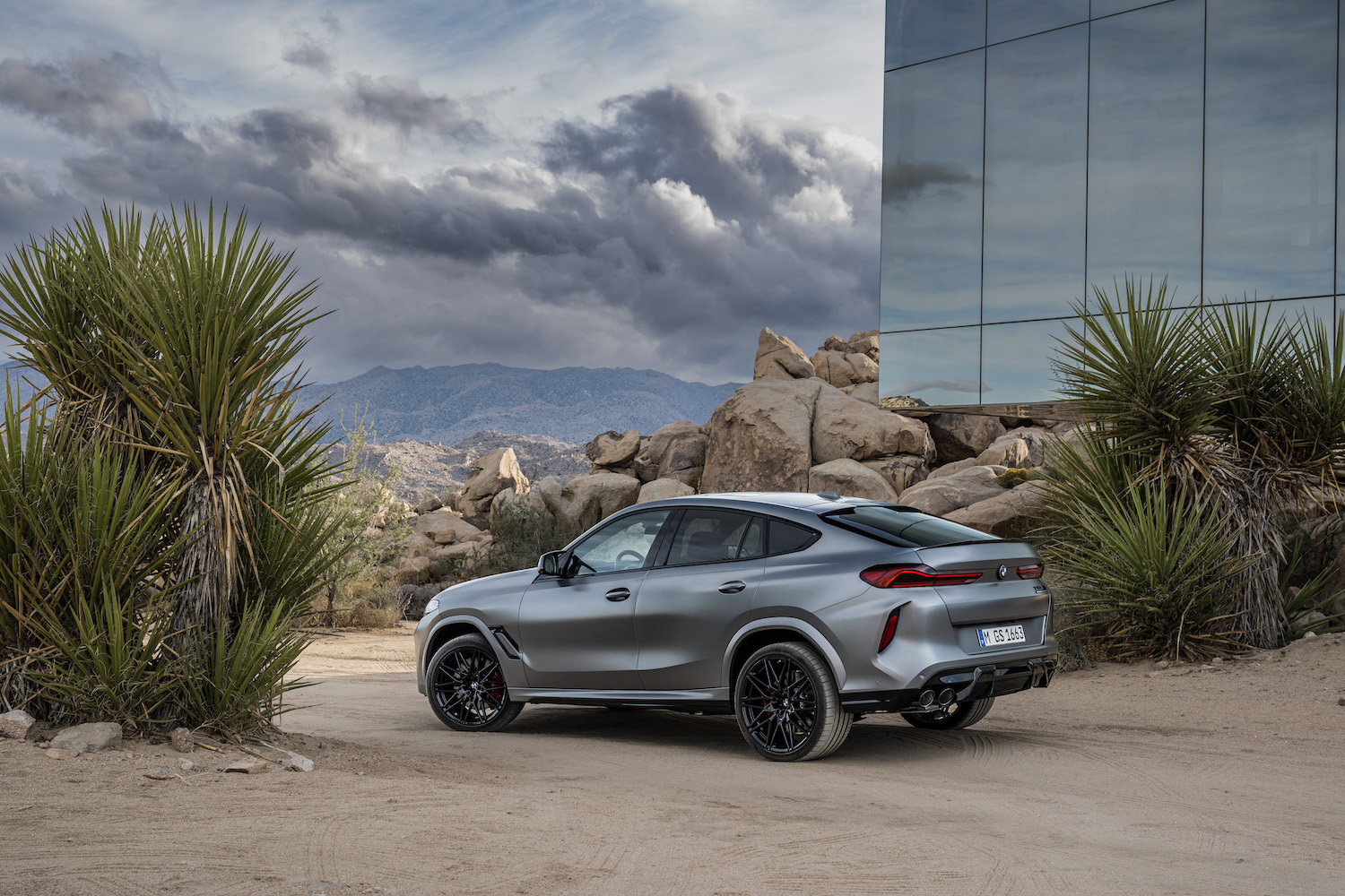 Rear end angle of the 2024 BMW X6 M Competition parked in front of a glass building in the desert.