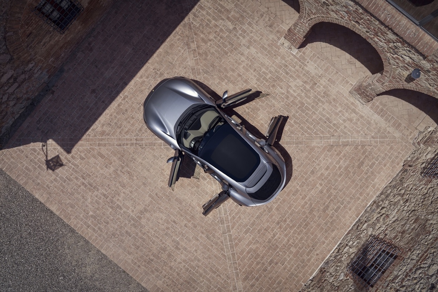 Overhead shot of the 2024 Ferrari Purosangue with all of the door opens in a stone parking lot.