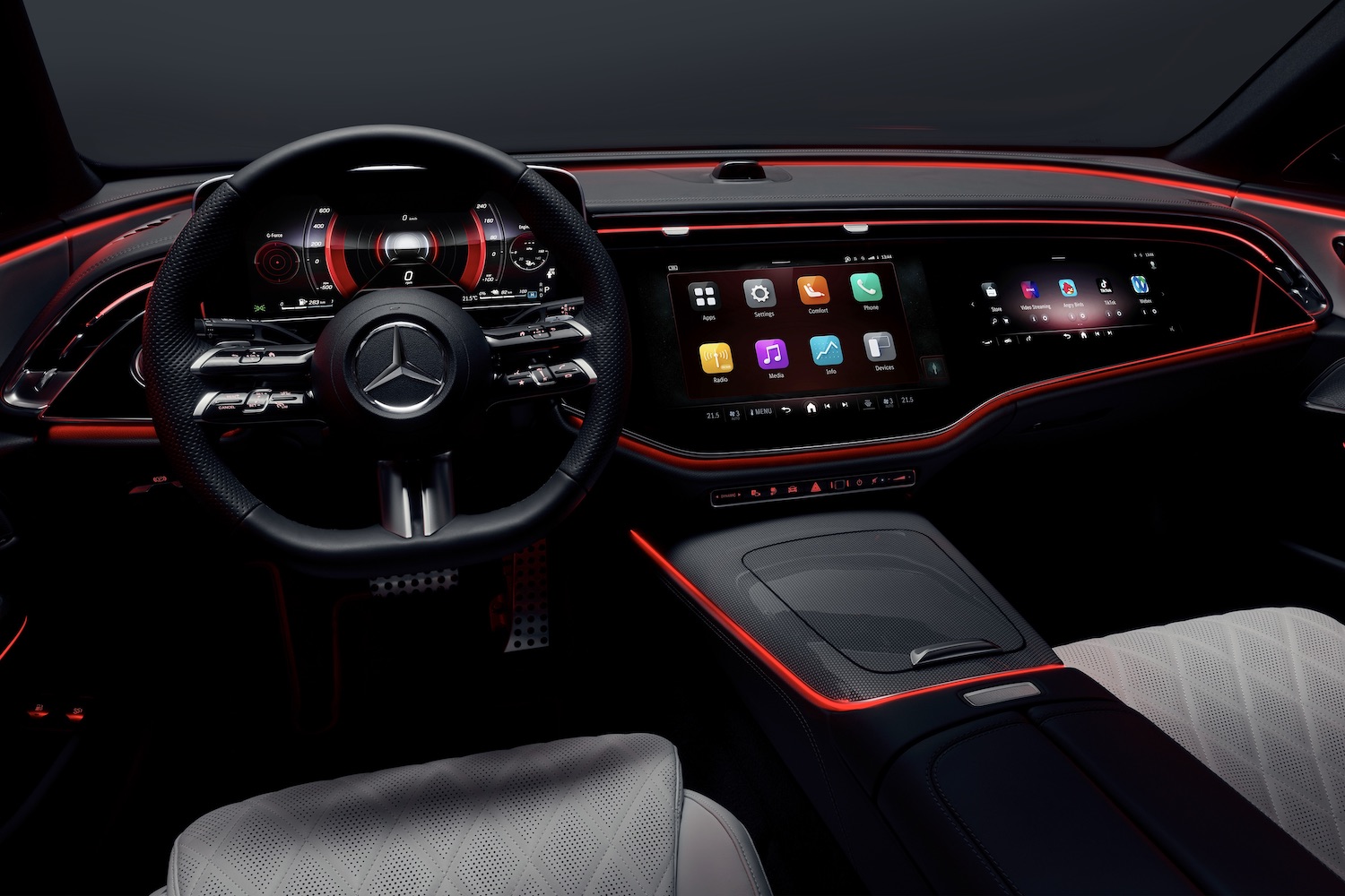 Close up of dashboard and steering wheel in the 2024 Mercedes-Benz E-Class Superscreen from the driver's seat with red lighting.