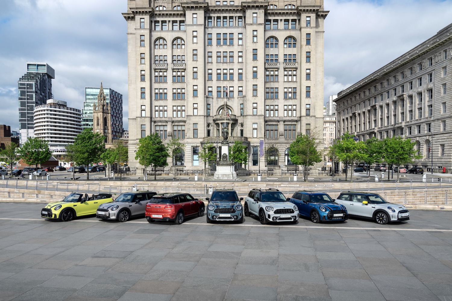 2024 Mini Cooper Family parked outside in a line in front of an old British building with clouds in the back.