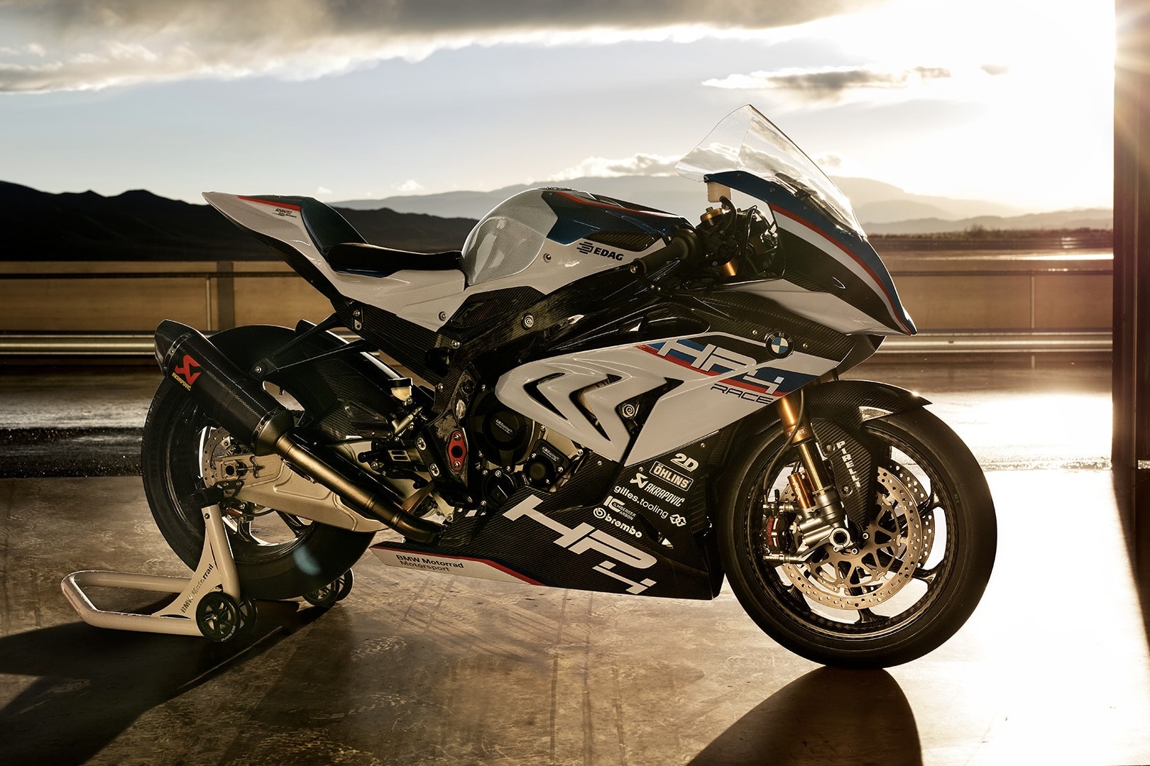 BMW HP4 Race parked in a garage at a race track with the sun setting in the back.
