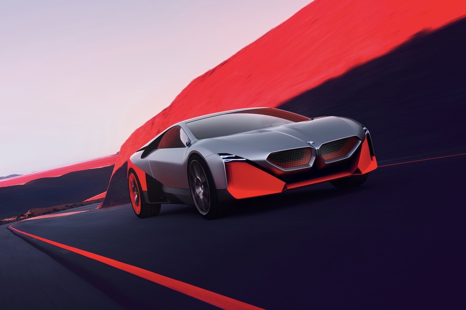 BMW M Vision NEXT Concept driving down the road from passenger's side front end angle in front of red mountains.