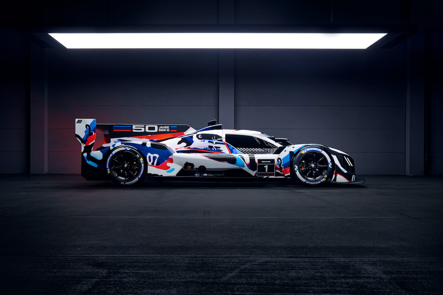 BMW M8 Hybrid V8 race car parked in a garage under a studio light side profile.