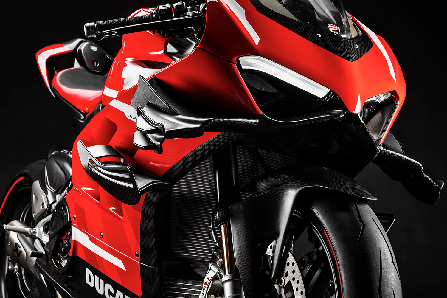 Close up of front end of Ducati Superleggera V4 with lights on and winglets in front of a black screen.