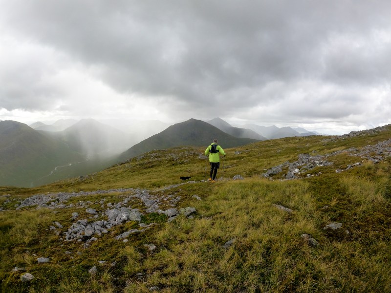 A man runs across the hills with a rainstorm forming behind.