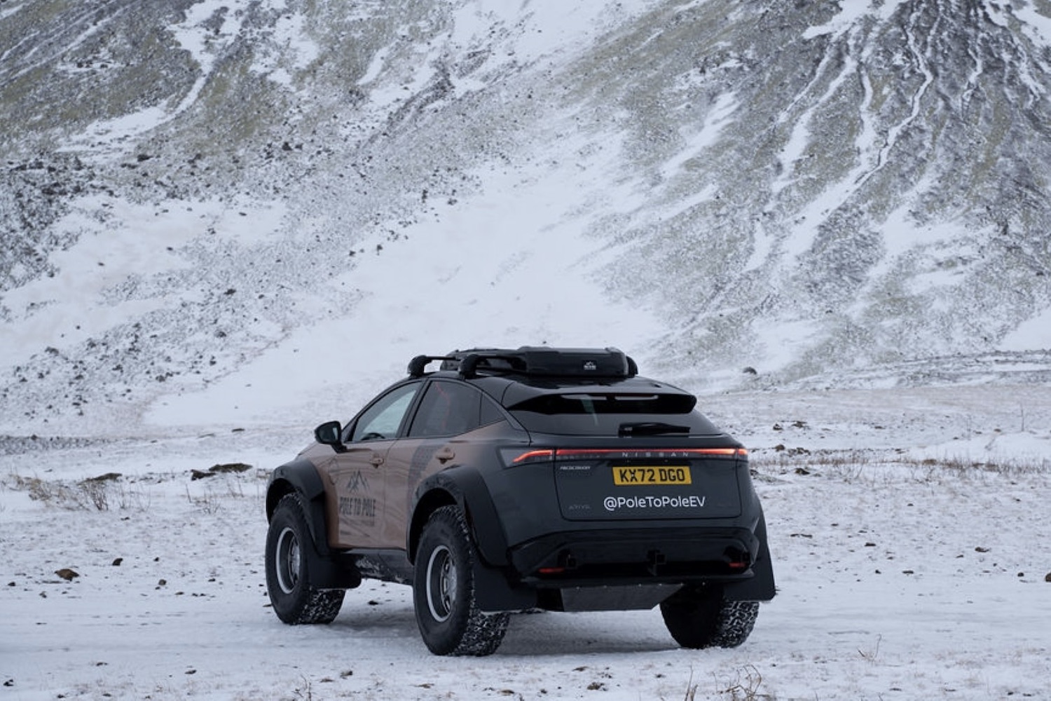 Rear end angle of the Nissan Ariya parked on snowy terrain with mountains in the back.