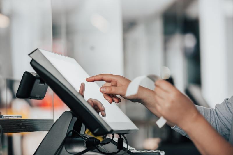 Clerk tapping touchscreen register while holding a receipt.
