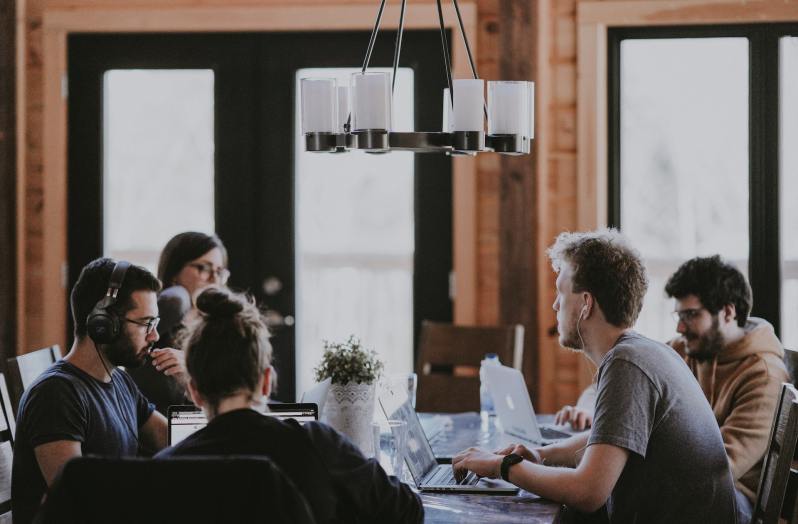 Group of people working on laptops at a communal table.