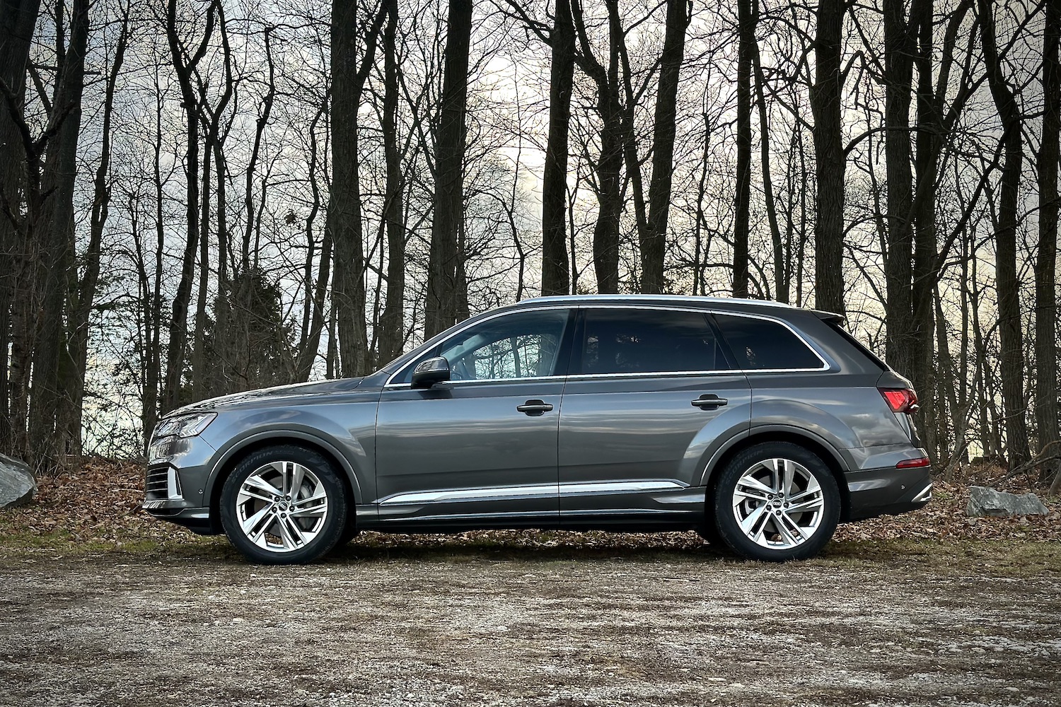 Side profile of the 2022 Audi Q7 Prestige parked on a gravel lot in front of trees.