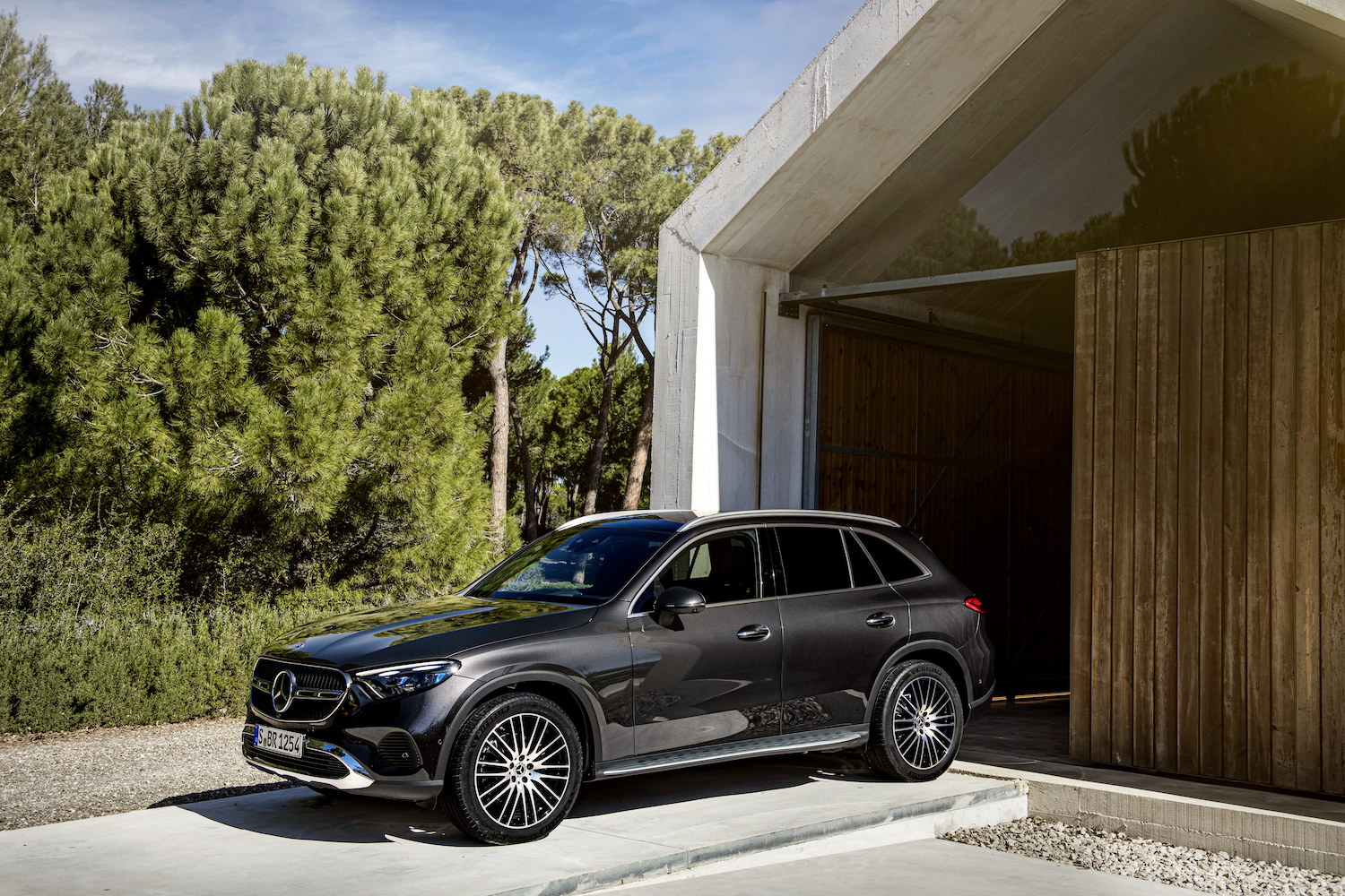 Front end angle of the 2023 Mercedes-Benz GLC parked in front of a garage with trees in the back.